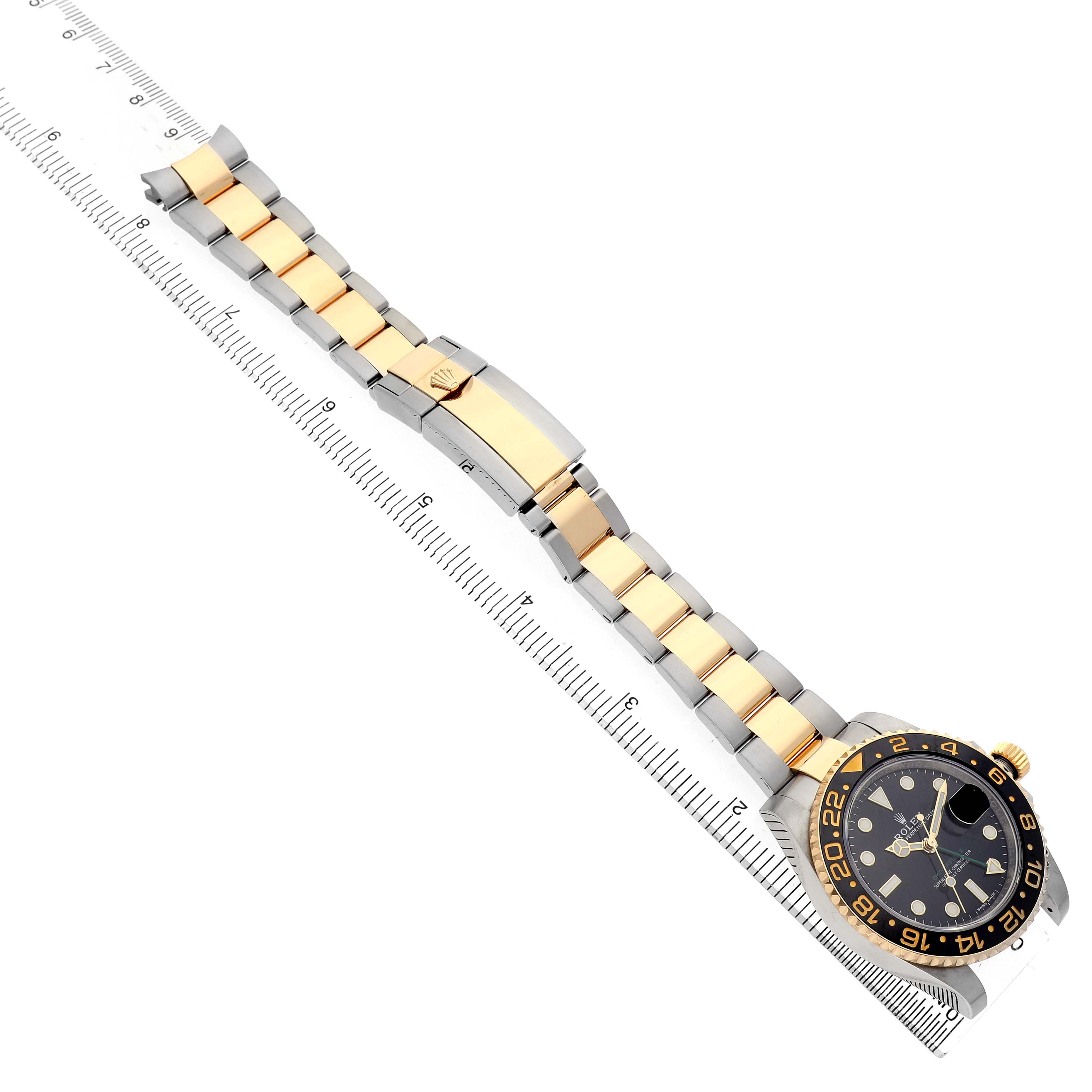 The Rolex GMT-Master 116713LN Men's Steel and Gold (two tone) Black Dial watch is shown from an overhead angle, highlighting its dial, bezel, and two-tone bracelet along a ruler.