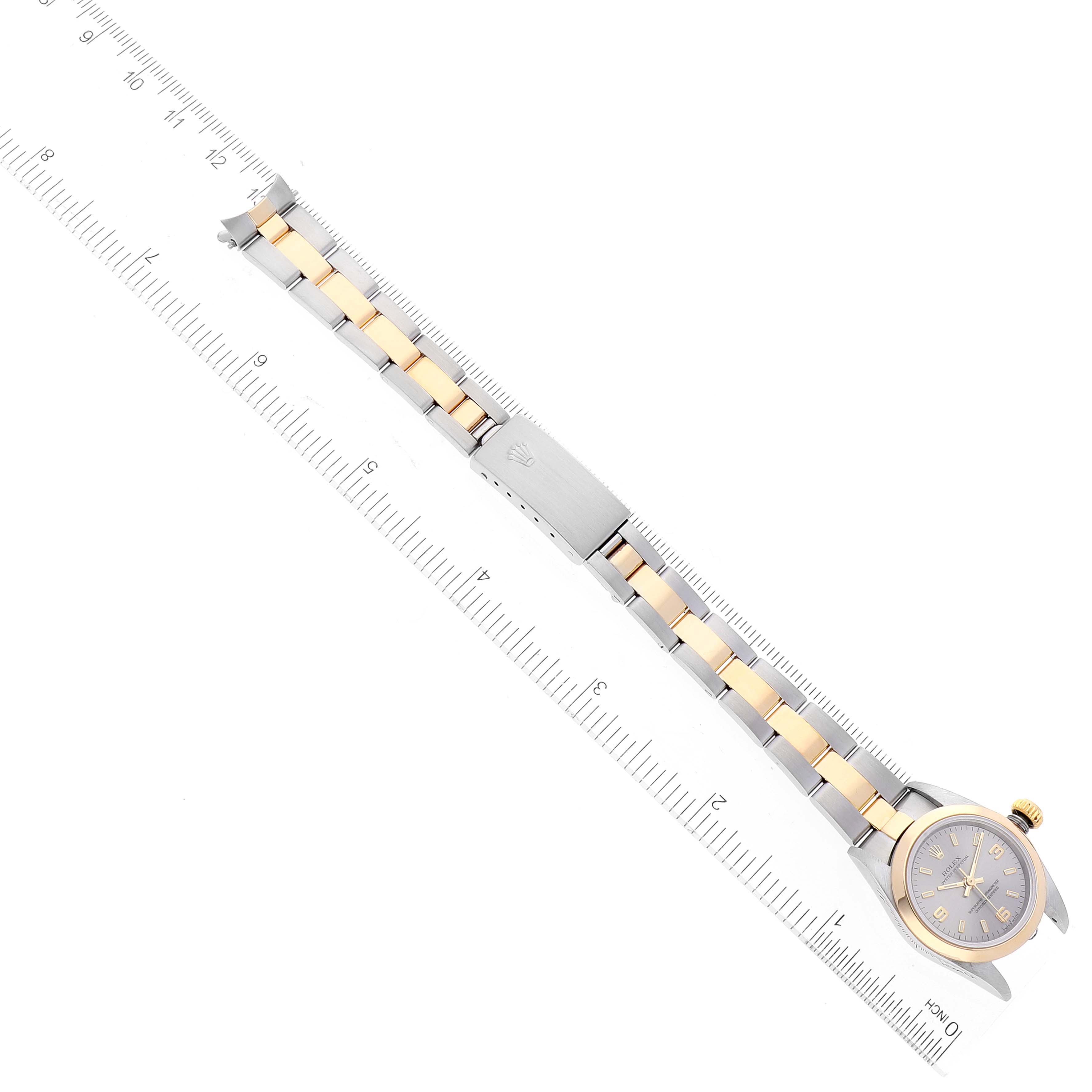 The image shows an aerial view of a Rolex Oyster Perpetual 76183 Women's Steel and Gold (two tone) Grey Dial 76183 Women's Steel and Gold (two tone) Grey Dial watch, highlighting the dial, bracelet, and clasp alongside a ruler for scale.