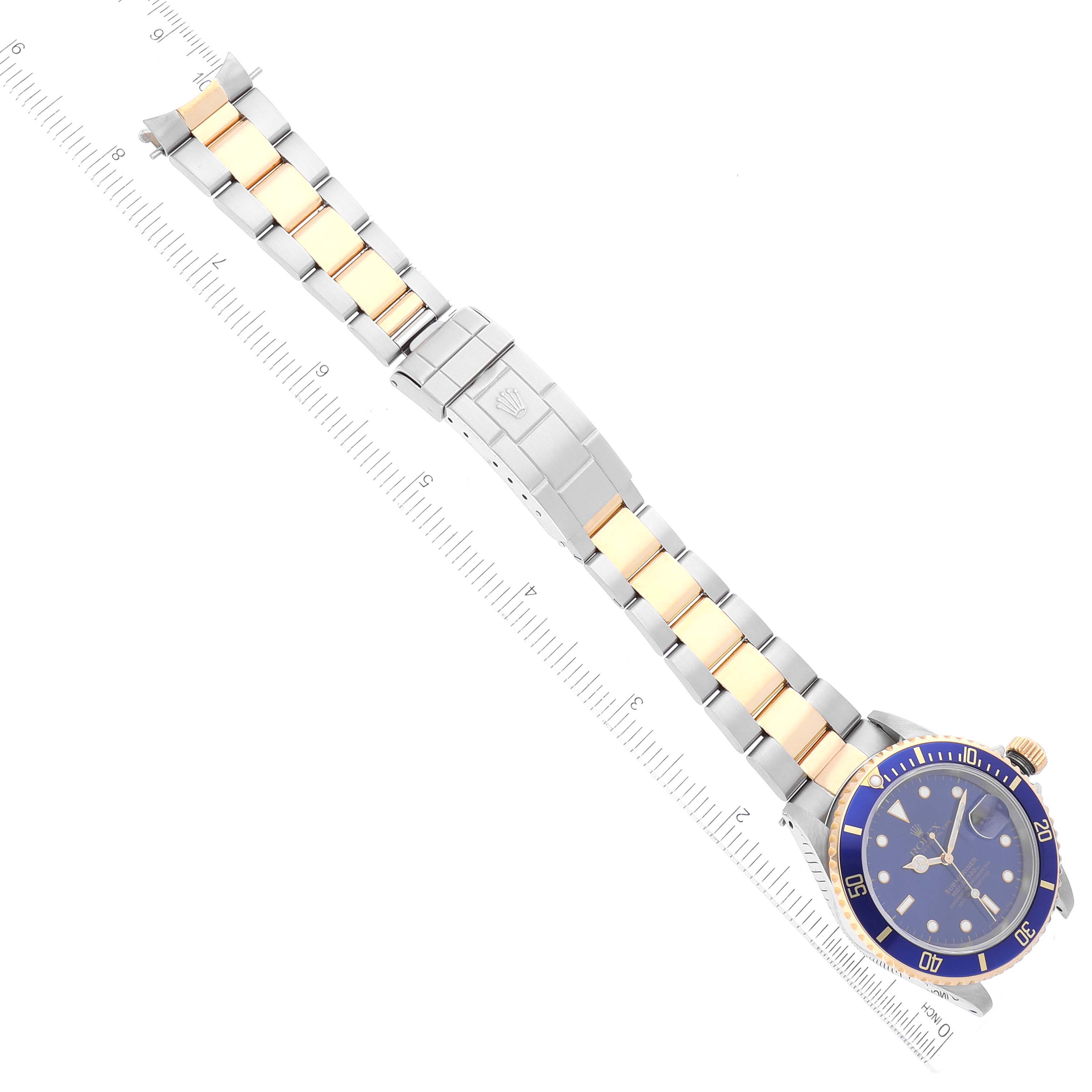 This image shows an aerial view of a Rolex Submariner 16613 Men's Steel and Gold (two tone) Blue Dial 16613 Men's Steel and Gold (two tone) Blue Dial watch with a blue bezel and a two-tone metal bracelet, positioned next to a ruler.