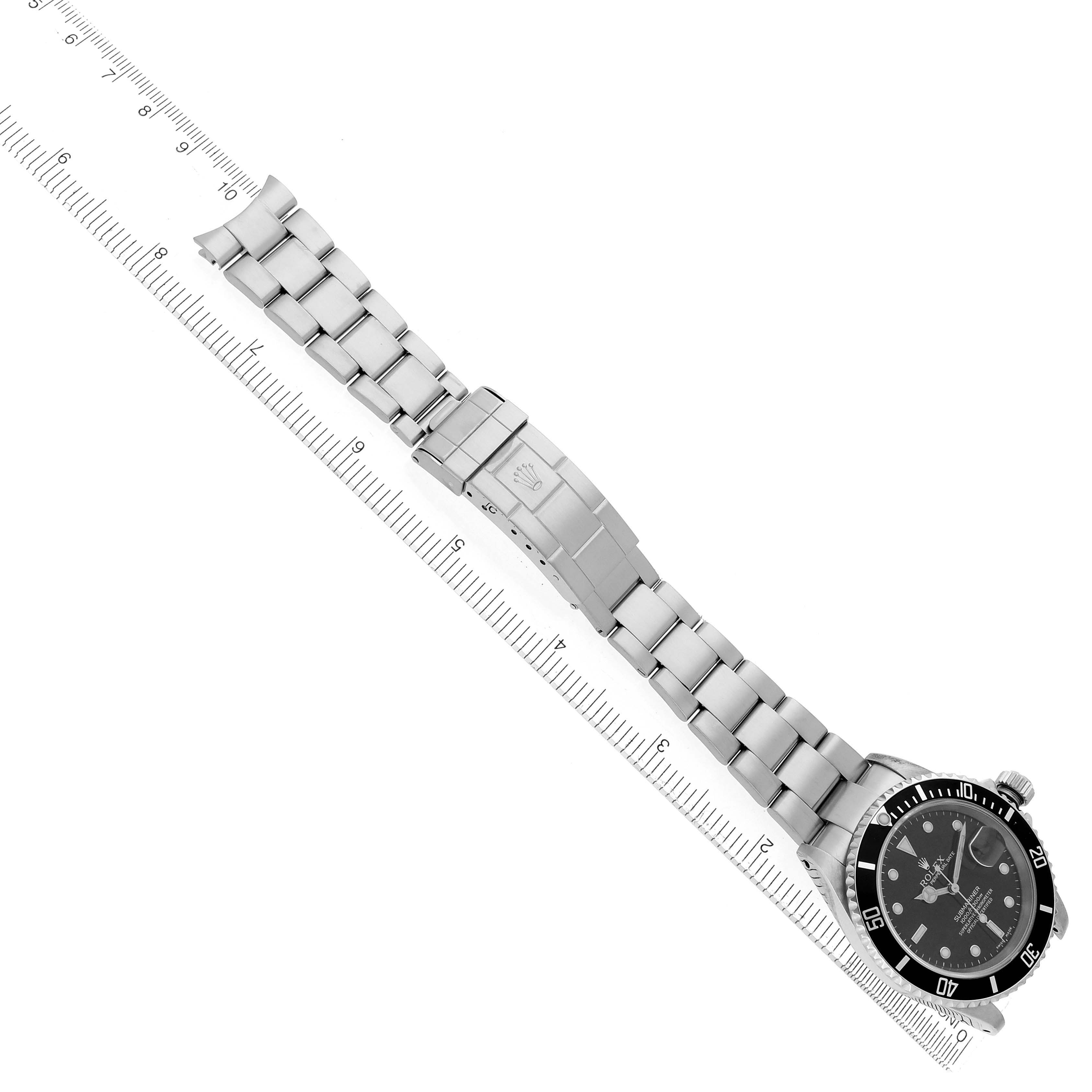 The image shows a Rolex Submariner model 16610 men
s watch laid flat with the bracelet extended next to a ruler, displaying its full length and the watch face.