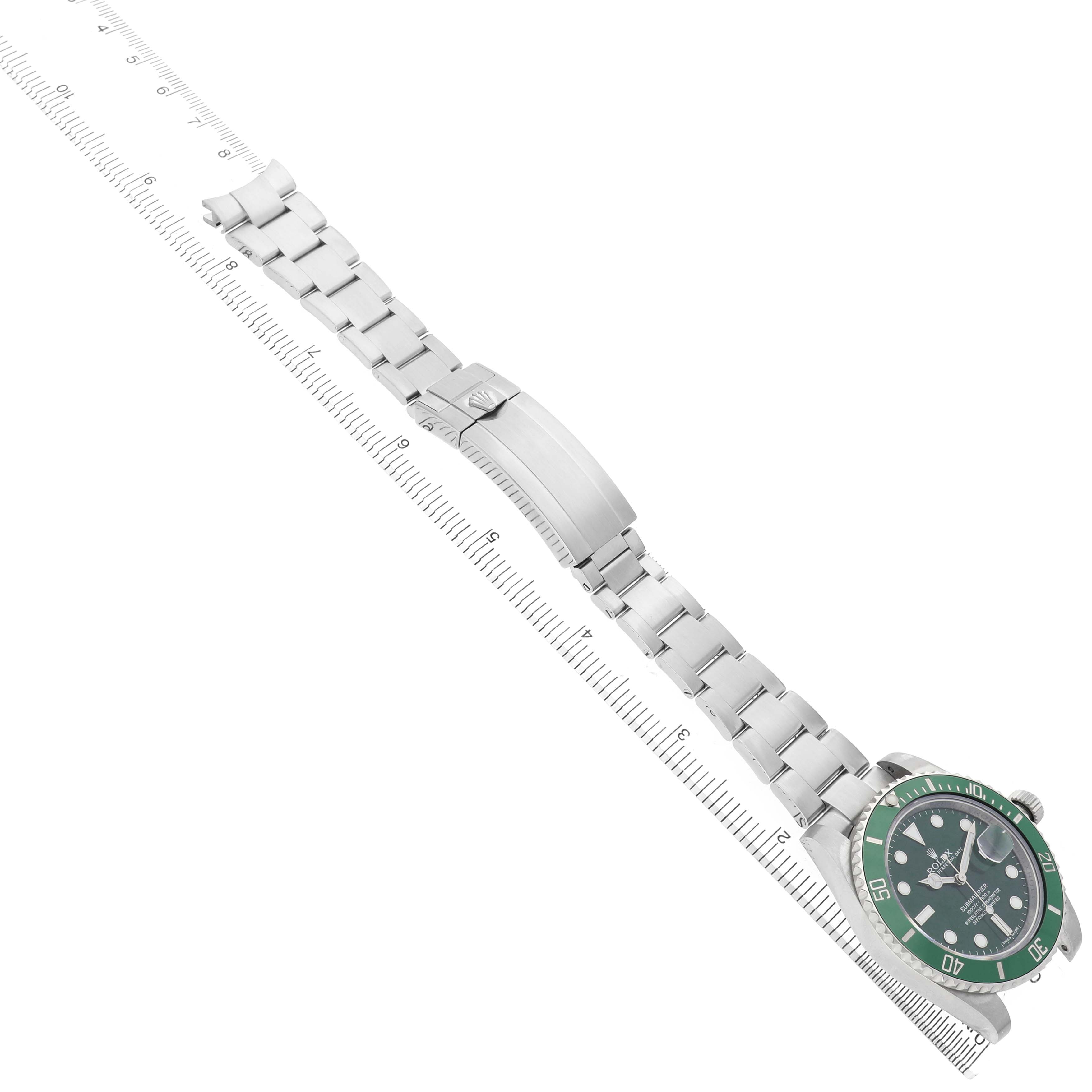 The Rolex Submariner 116610LV Men's Stainless Steel Green Dial watch is shown from a top-down angle, displaying its green bezel, dial, and link bracelet alongside a ruler.