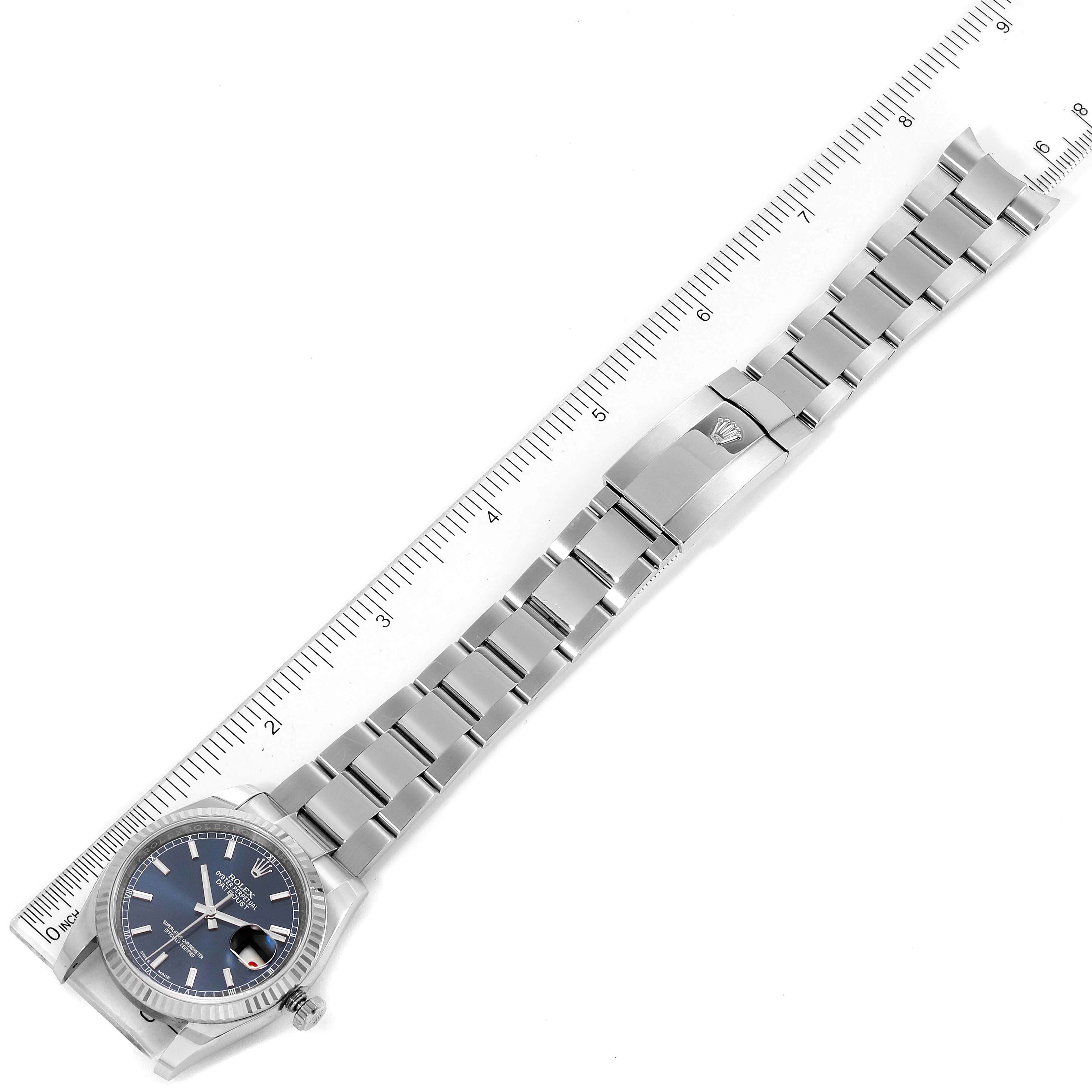 The image shows the top view of a Rolex Datejust 116234 Men's Stainless Steel Blue Dial 116234 Men's Stainless Steel Blue Dial watch with the entire bracelet laid out next to a ruler.