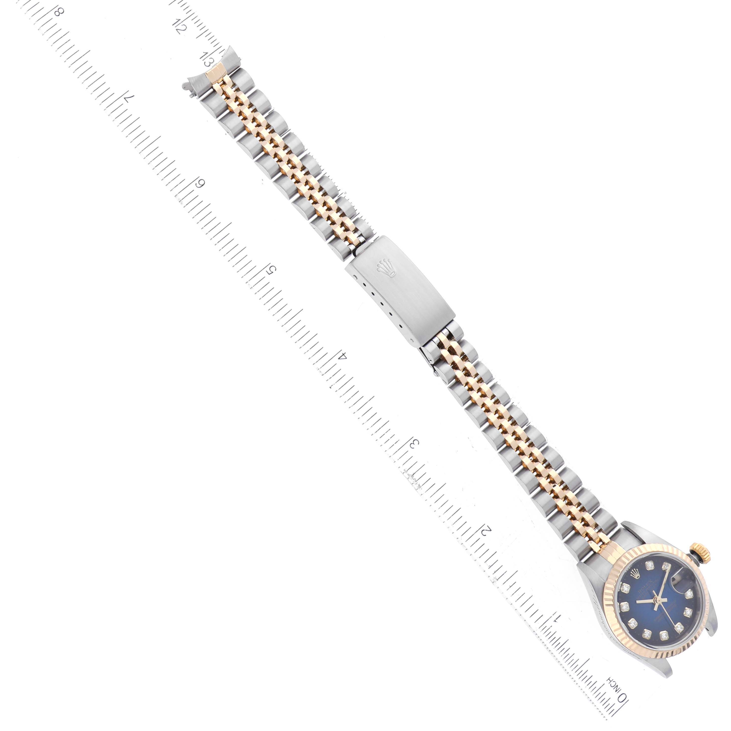 The image shows a Rolex Datejust 79173 Women's Steel and Gold (two tone) Blue Dial 79173 Women's Steel and Gold (two tone) Blue Dial watch laid flat with a metal strap, featuring a blue dial and gold accents, aligned diagonally with a ruler.