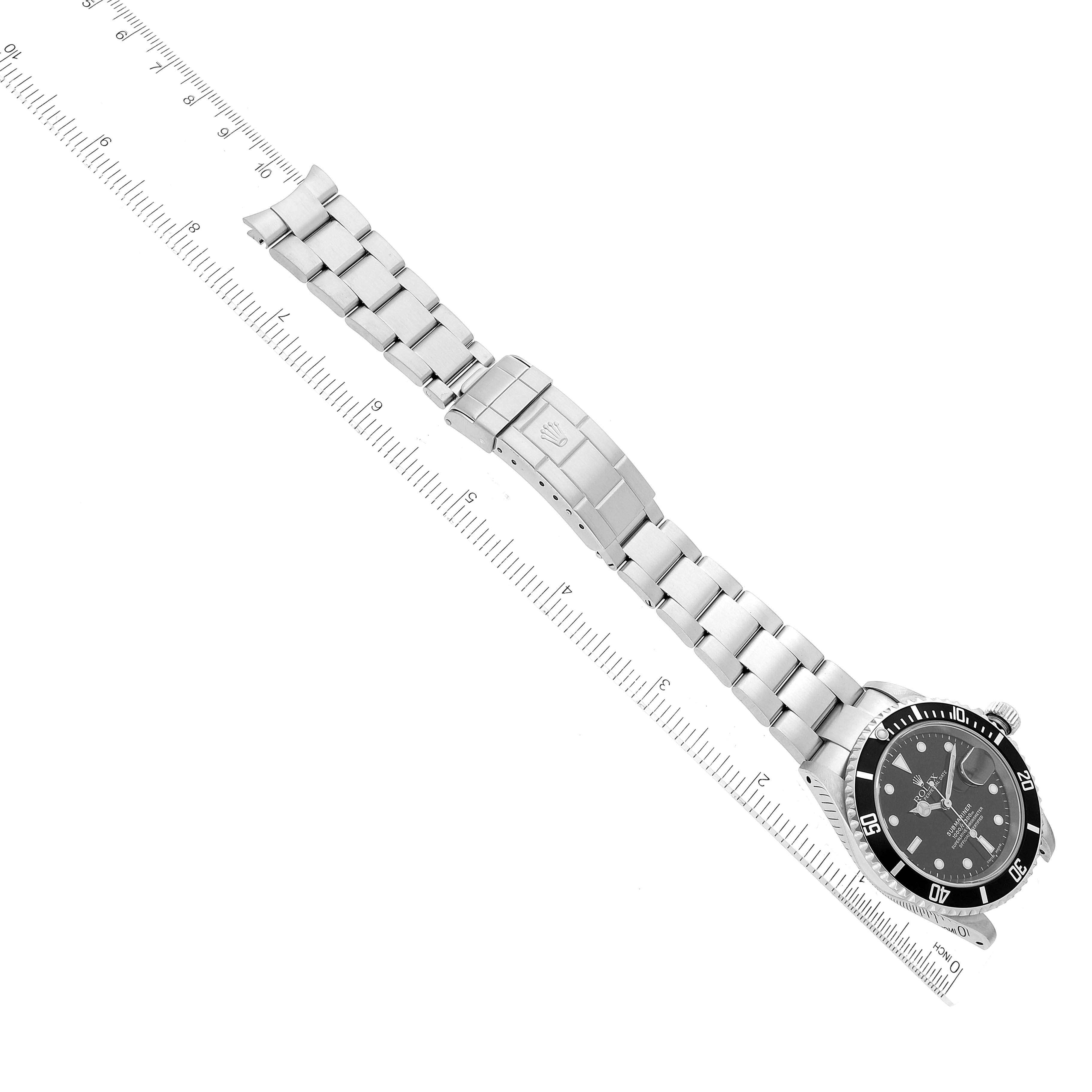 This is a top-view image of a Rolex Submariner 16610 Men
s Stainless Steel Black Dial 16610 Men
s Stainless Steel Black Dial watch, showing the face, bezel, and full bracelet against a measurement scale.
