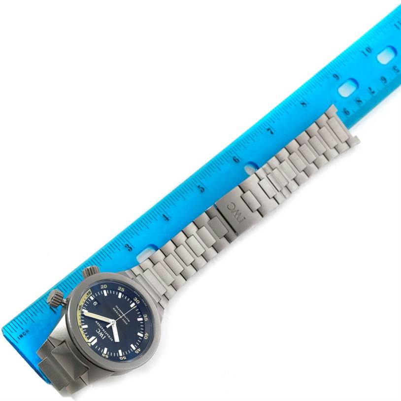 The image shows an IWC Aquatimer IW356802 Men's Titanium Black Dial IW356802 Men's Titanium Black Dial watch placed flat next to a blue ruler, displaying its face, bezel, crown, and metal bracelet.