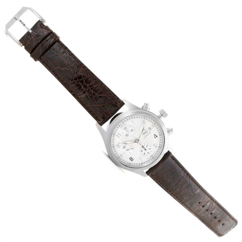 The image shows an angled view of an IWC Pilot IW325110 Men's Stainless Steel Silver Dial IW325110 Men's Stainless Steel Silver Dial model watch, highlighting its brown leather strap and silver dial with chronograph subdials.