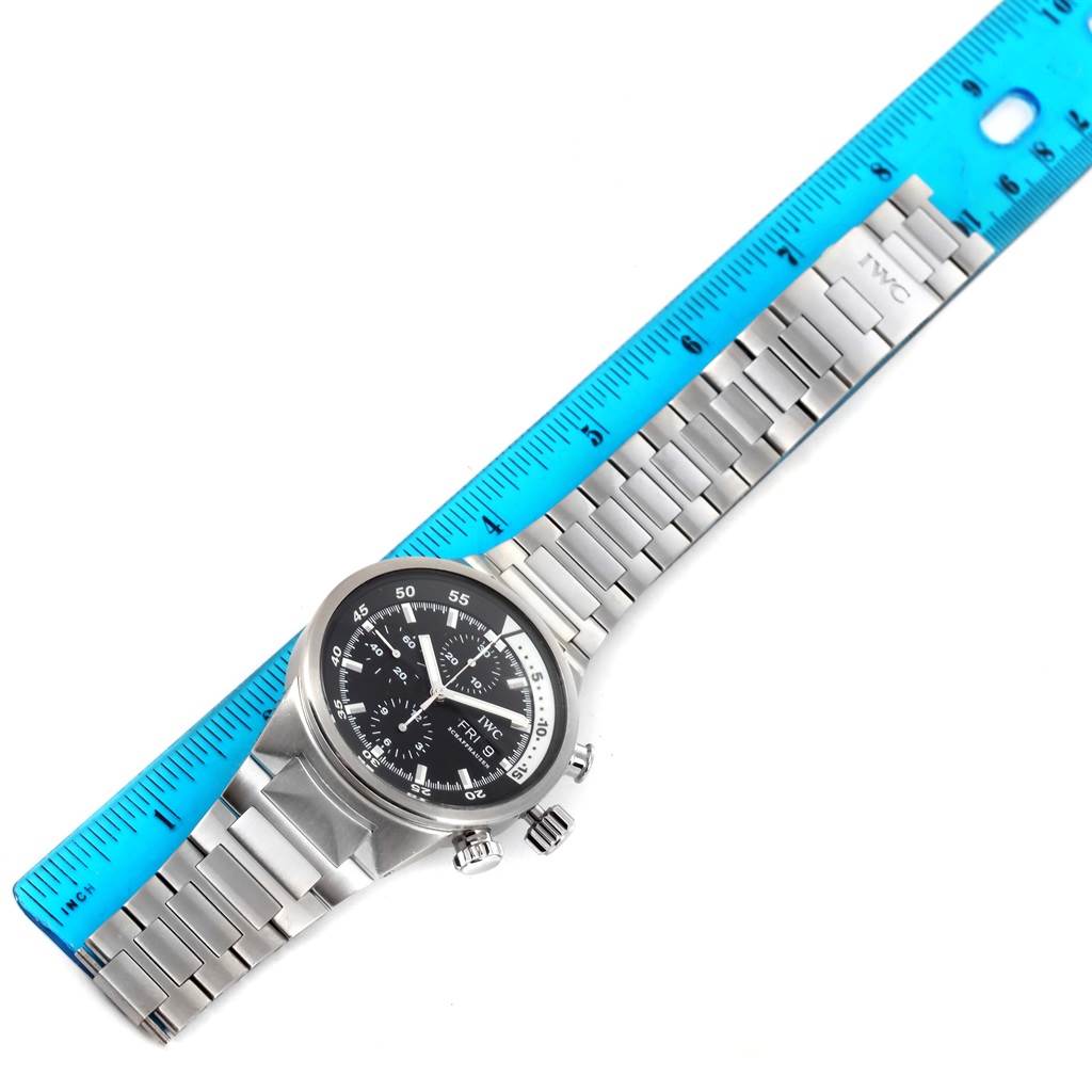 The image shows the IWC Aquatimer IW371928 Men's Stainless Steel Black Dial IW371928 Men's Stainless Steel Black Dial watch from an overhead angle, highlighting its stainless steel band and dial alongside a blue ruler.