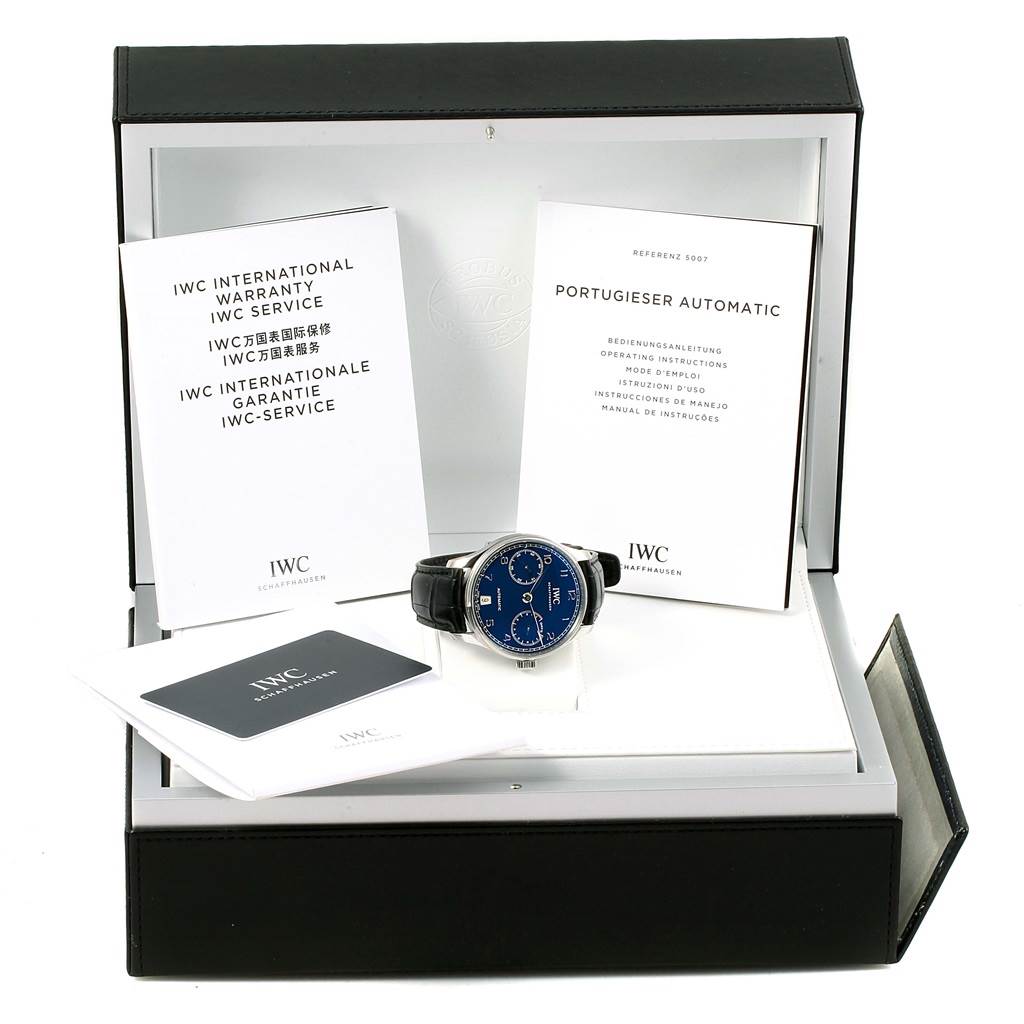 The image shows an IWC Portuguese IW500710 Men's Stainless Steel Blue Dial IW500710 Men's Stainless Steel Blue Dial watch with a blue dial, black strap, warranty cards, and manual, all inside the watch box.