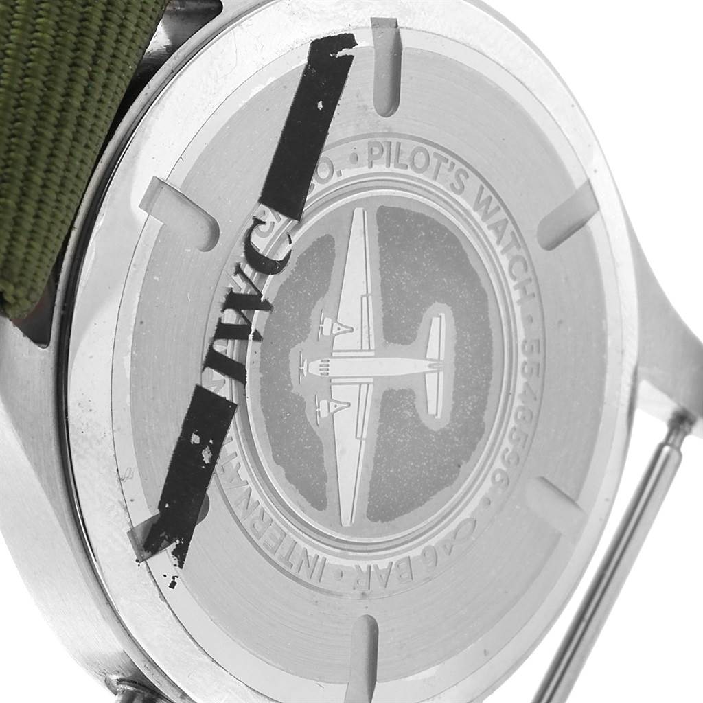 The image shows the case back of an IWC Pilot IW327011 Men's Stainless Steel Black Dial IW327011 Men's Stainless Steel Black Dial watch, featuring an engraved airplane and part of the green strap.