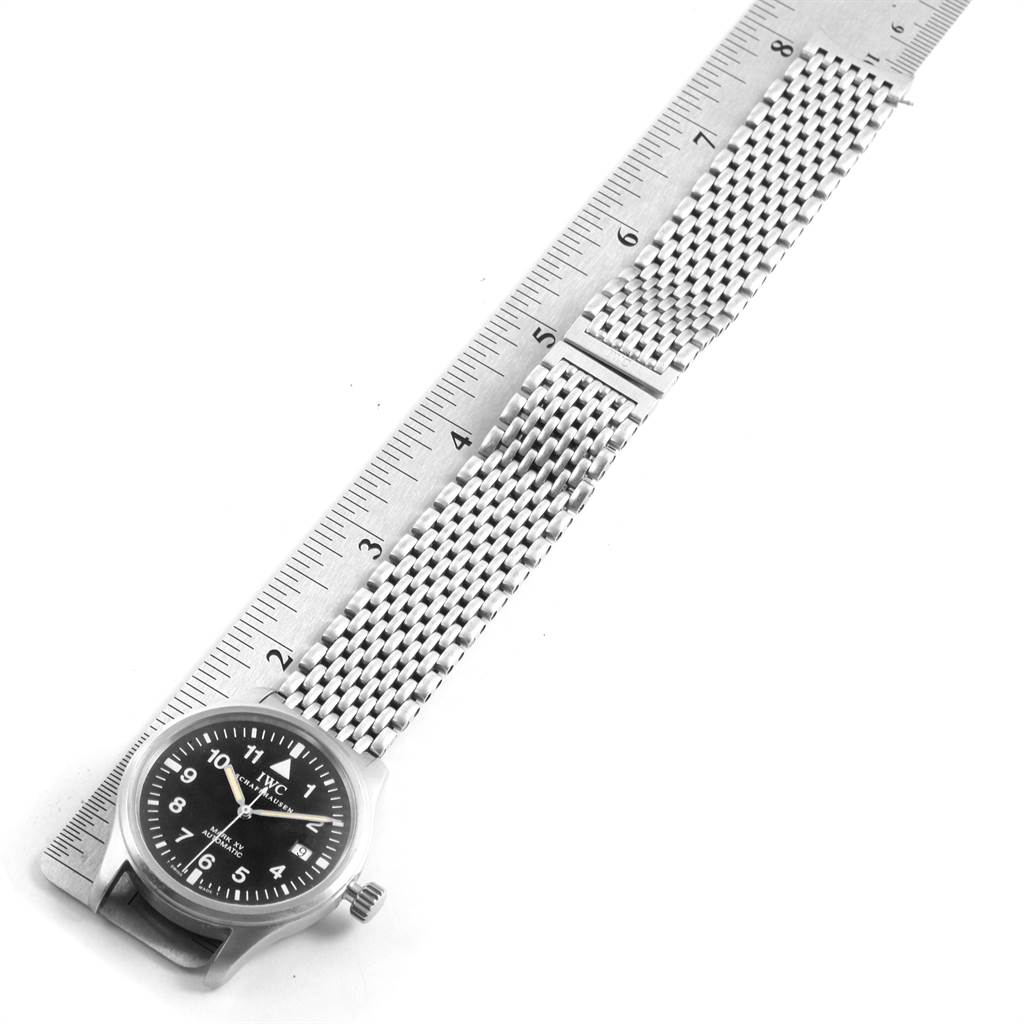 The image shows an IWC Pilot IW325301 Men's Stainless Steel Black Dial IW325301 Men's Stainless Steel Black Dial model watch from a top-down angle, highlighting its face and extended metal band next to a ruler.