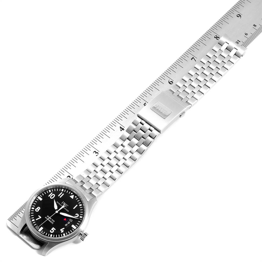 The image shows the IWC Pilot IW326504 Men's Stainless Steel Black Dial IW326504 Men's Stainless Steel Black Dial model watch laid flat, displaying its face, stainless steel bracelet, and clasp next to a ruler.