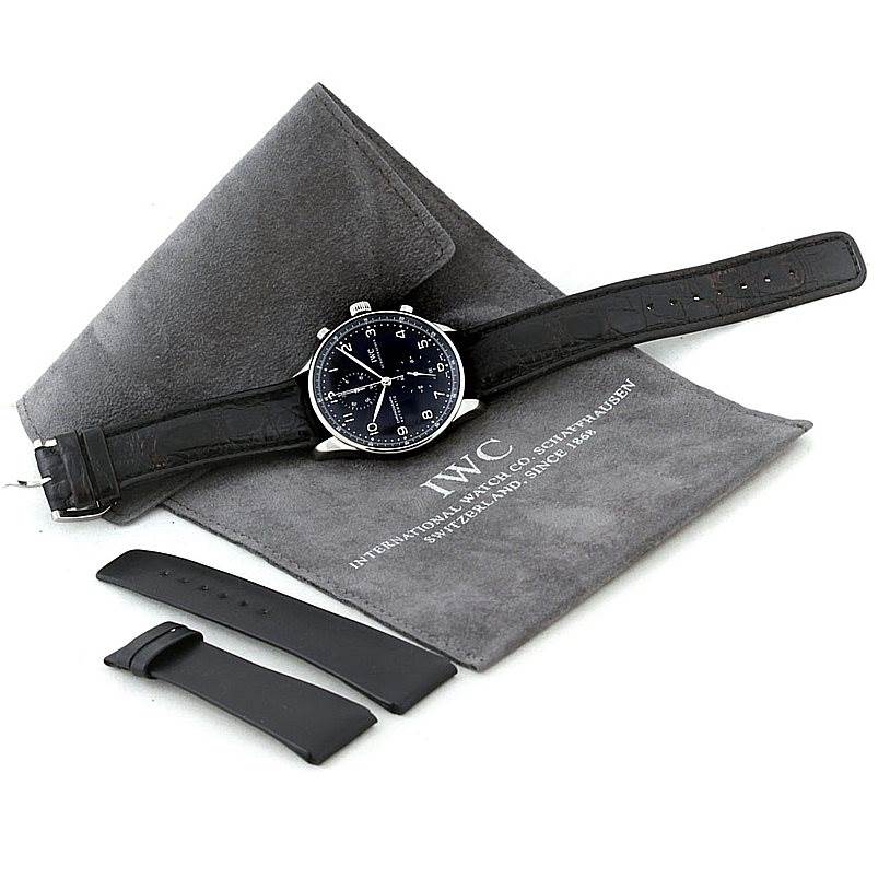 The image shows an IWC Portuguese IW371438 Men
s Stainless Steel Black Dial IW371438 Men
s Stainless Steel Black Dial watch with a black strap, laid on a grey case, along with spare black strap segments.