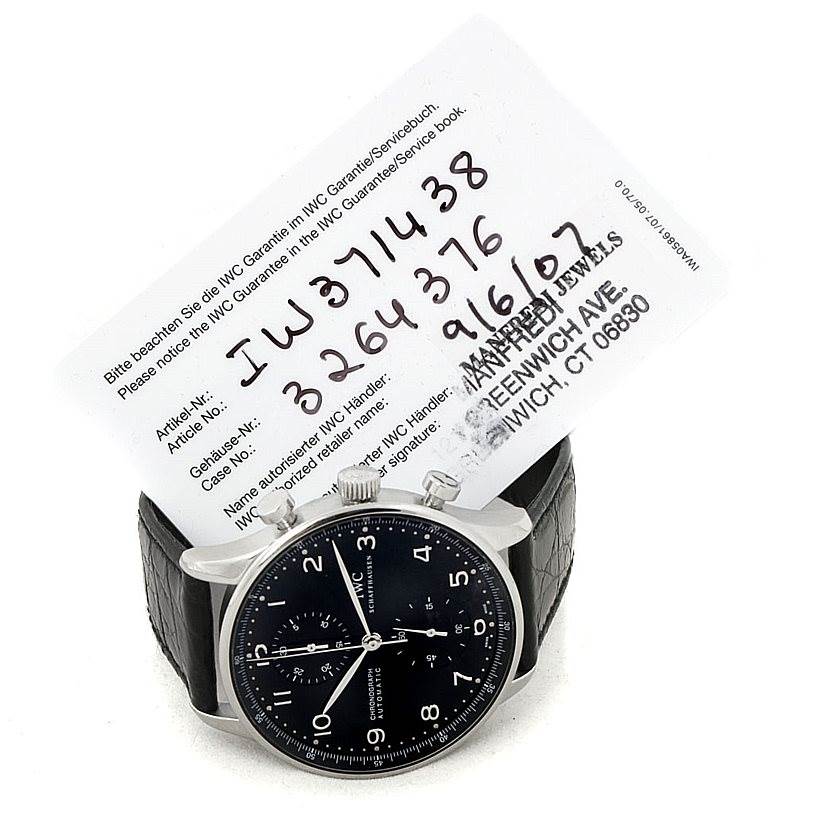 The image shows an IWC Portuguese IW371438 Men's Stainless Steel Black Dial IW371438 Men's Stainless Steel Black Dial model watch from a front angle, displaying the dial, crown, and chronograph pushers along with a warranty card.