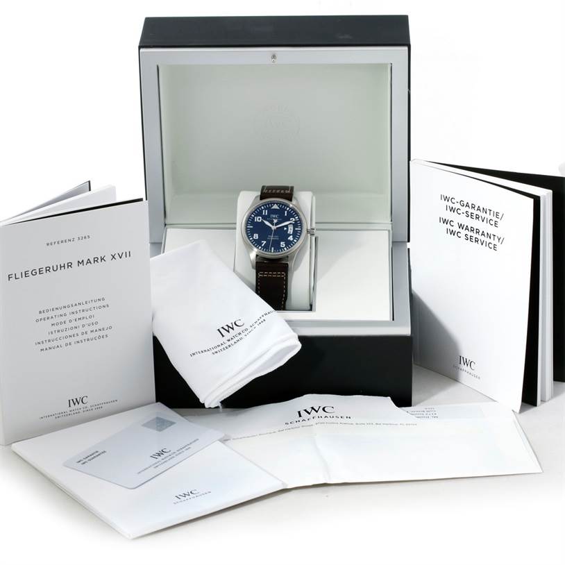 The IWC Pilot IW326506 Men's Stainless Steel Blue Dial IW326506 Men's Stainless Steel Blue Dial model watch is shown front-on in its box, accompanied by manuals, a cleaning cloth, and warranty booklets.