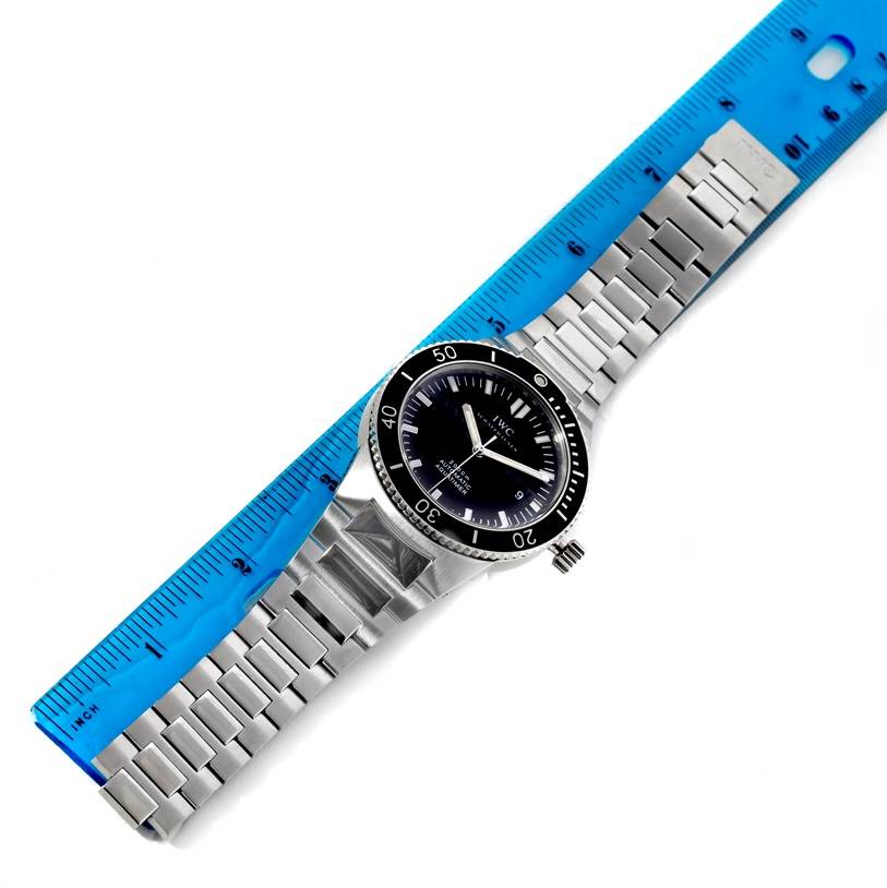 The IWC GST IW353602 Men's Stainless Steel Black Dial IW353602 Men's Stainless Steel Black Dial watch is shown from a top-down angle, displaying its face, bezel, crown, and metal bracelet against a blue ruler.