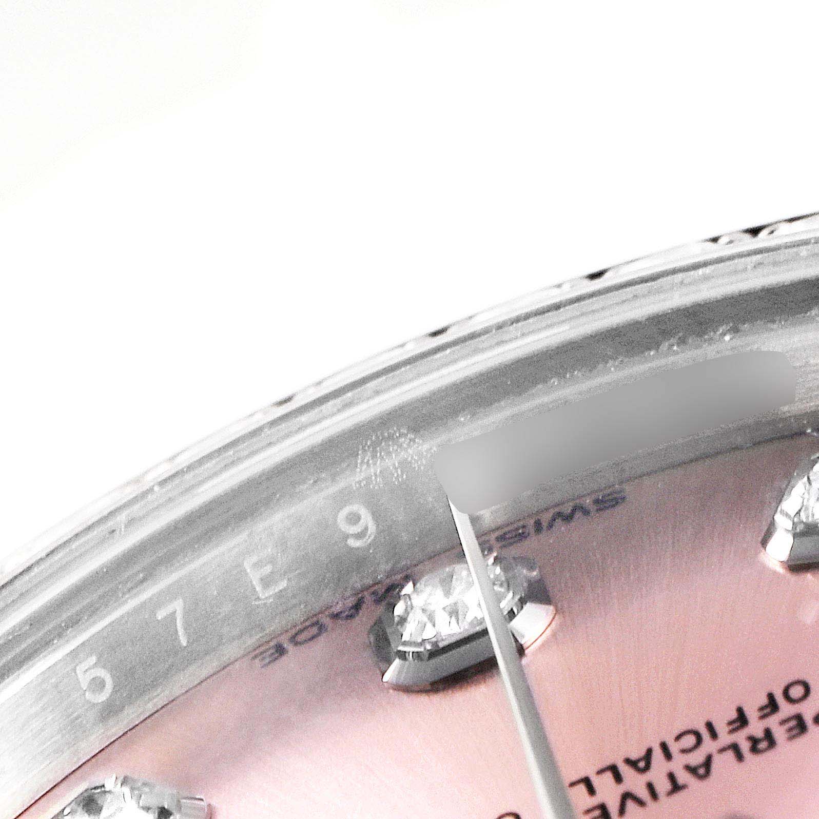 The image shows a close-up of the Rolex Mid-Size 178384 Women's Stainless Steel Pink Dial 178384 Women's Stainless Steel Pink Dial watch face, showcasing diamonds, text, and the edge of the bezel.