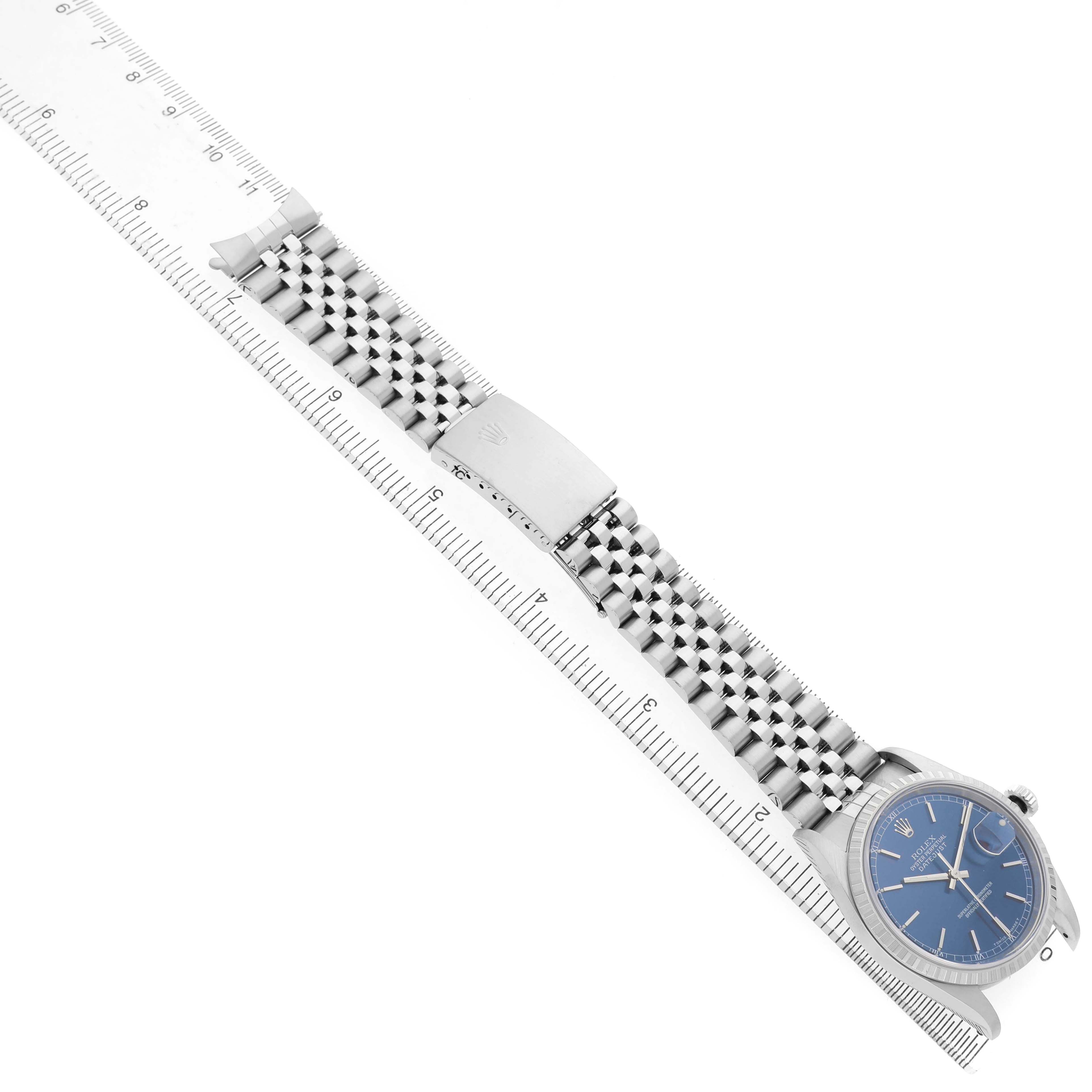 The image shows the Rolex Datejust 16220 Men's Stainless Steel Blue Dial watch diagonally aligned with a measuring ruler; displaying the bracelet, clasp, and face.