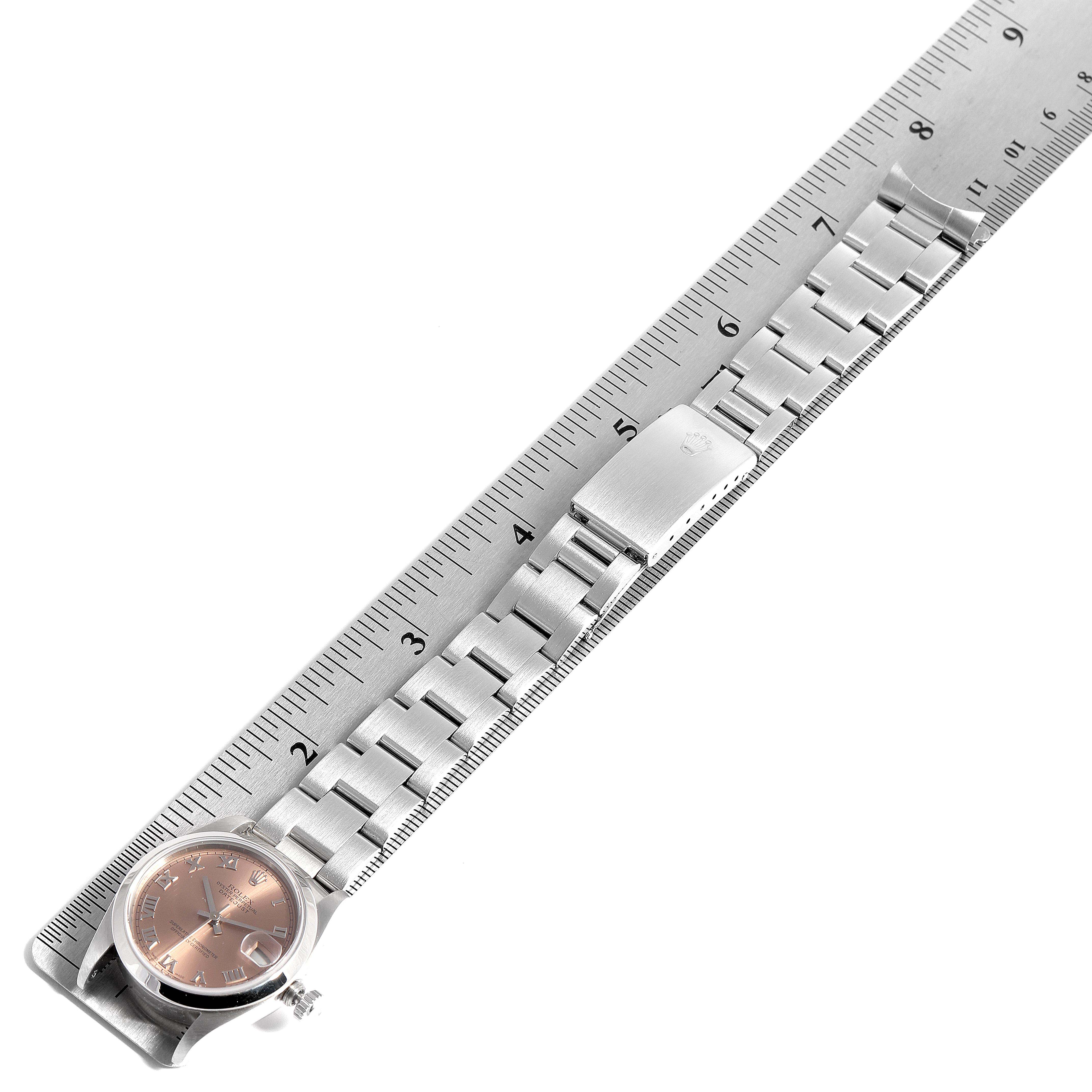 This image shows a Rolex Mid-Size 68240 Women
s Stainless Steel Pink Dial 68240 Women
s Stainless Steel Pink Dial watch laid flat alongside a ruler, displaying its face and bracelet.