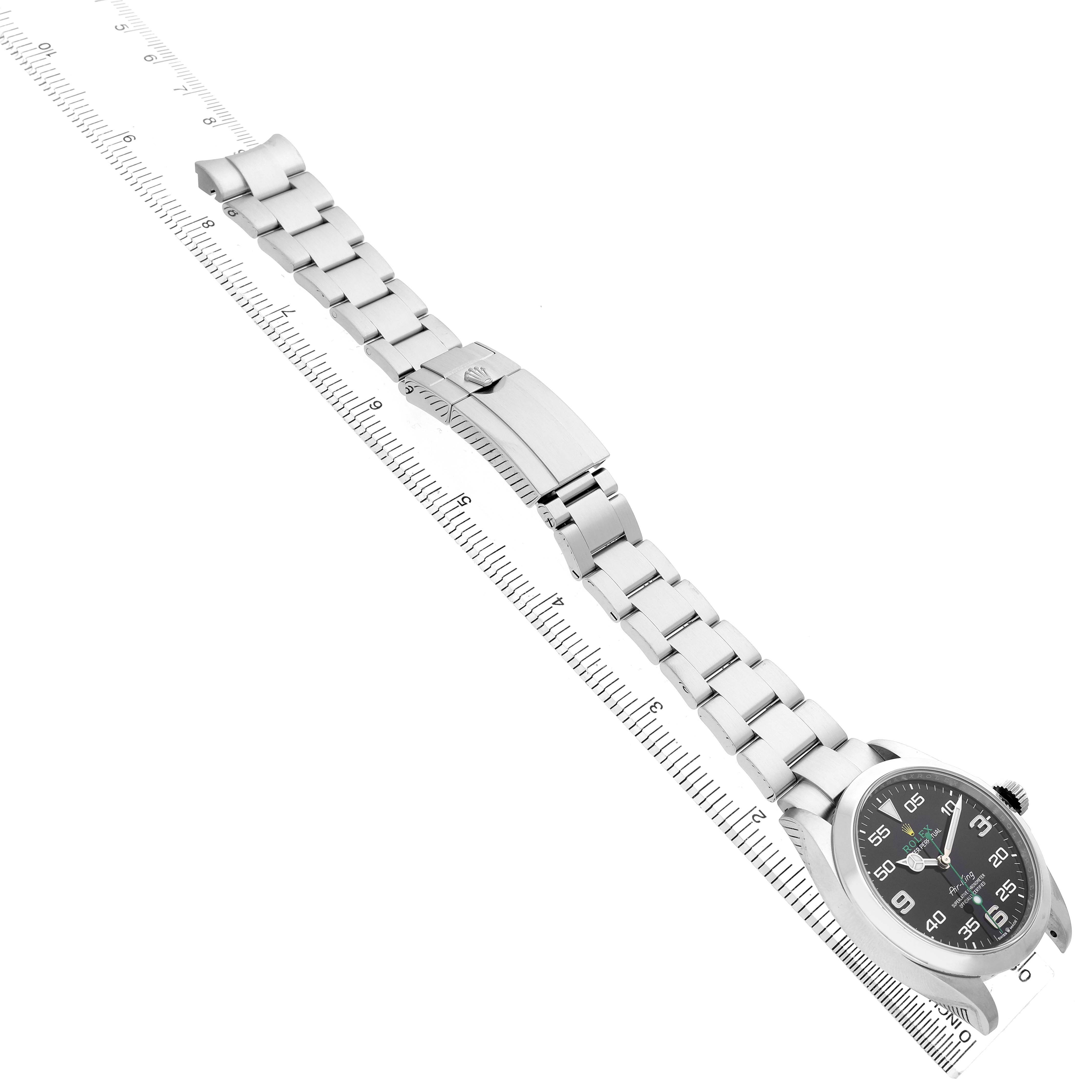 The Rolex Air-King 126900 Men's Stainless Steel Black Dial watch is shown from a side angle, displaying its bracelet and clasp along a ruler for scale.