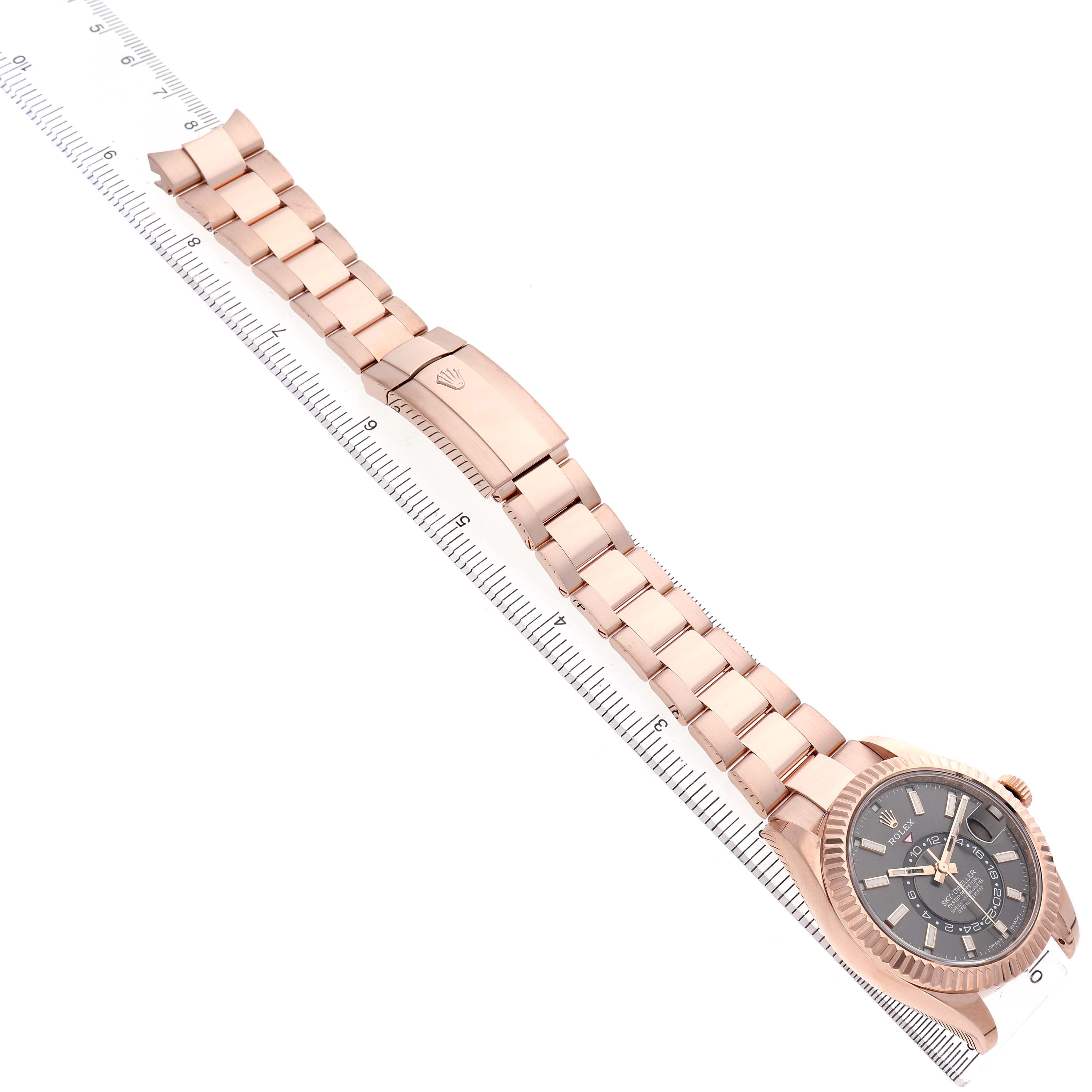 The Rolex Sky-Dweller 326935 Men's Rose Gold Grey Dial watch is shown at an angle with its bracelet extended and positioned alongside a ruler for scale.