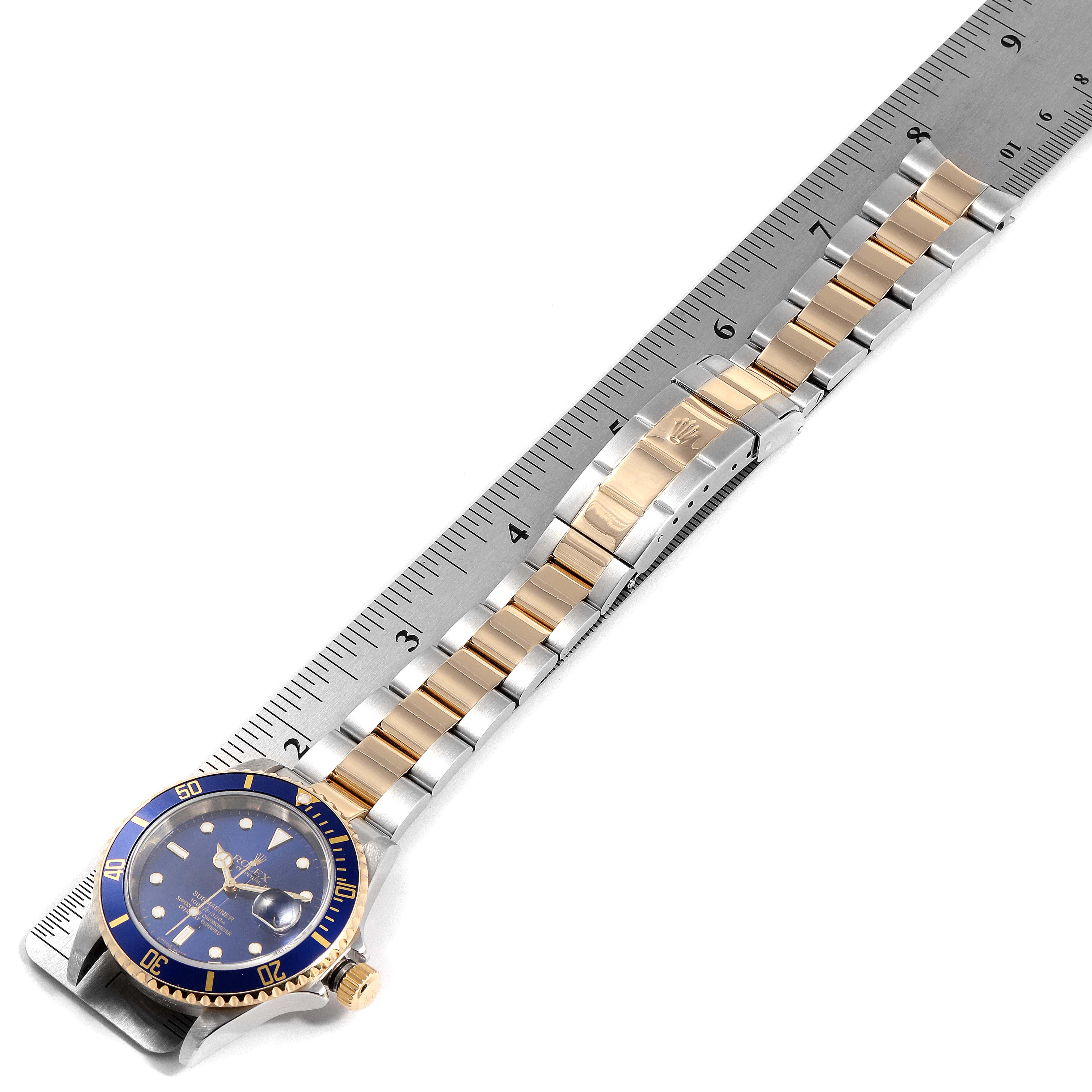 The image shows the Rolex Submariner 16613 Men
s Steel and Gold (two tone) Blue Dial 16613 Men
s Steel and Gold (two tone) Blue Dial watch from a top view, including the face, bezel, and full bracelet against a ruler for scale.