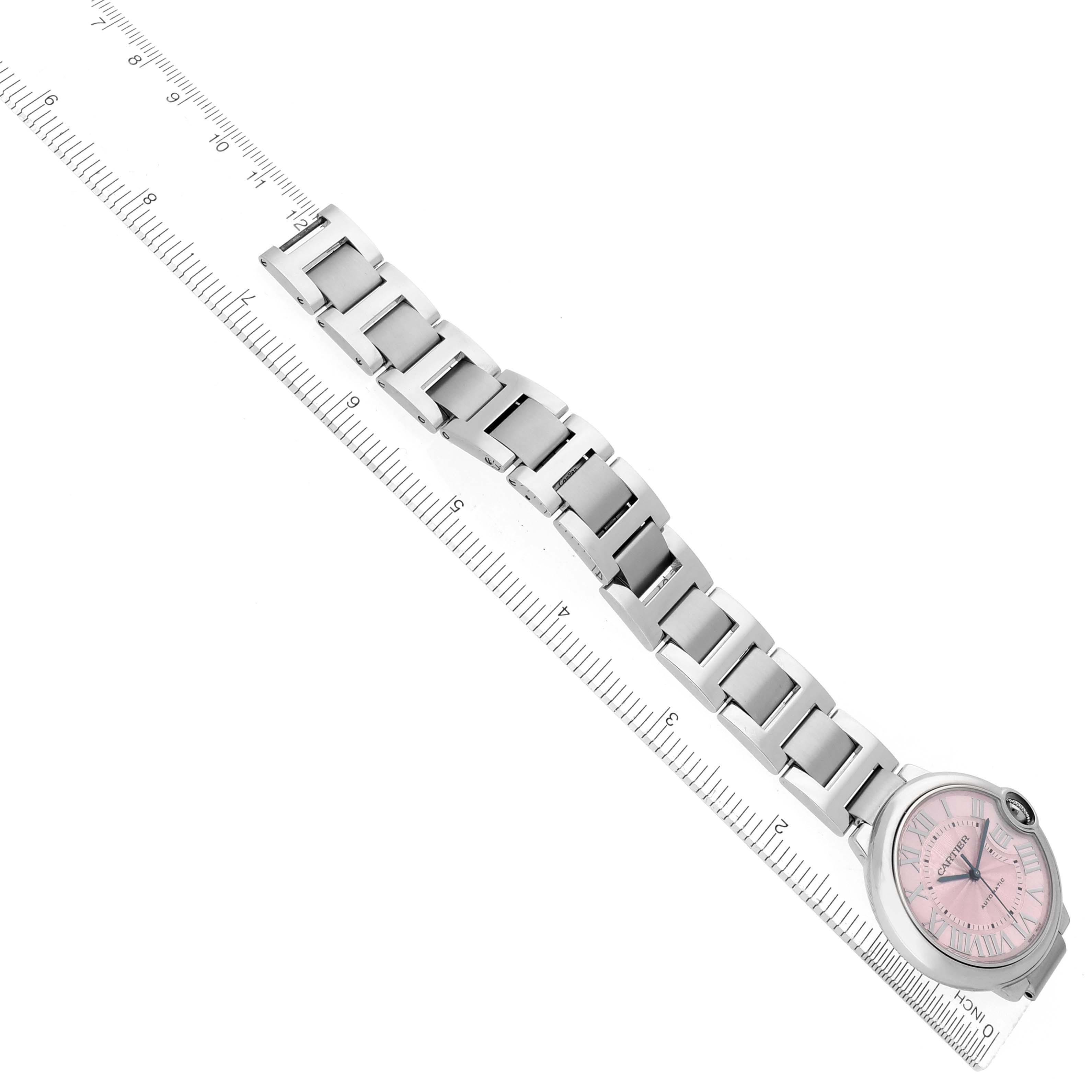The Cartier Ballon Bleu W6920041 Women's Stainless Steel Pink Dial watch is shown from a top-down angle, displaying its pink dial and full bracelet alongside a ruler.