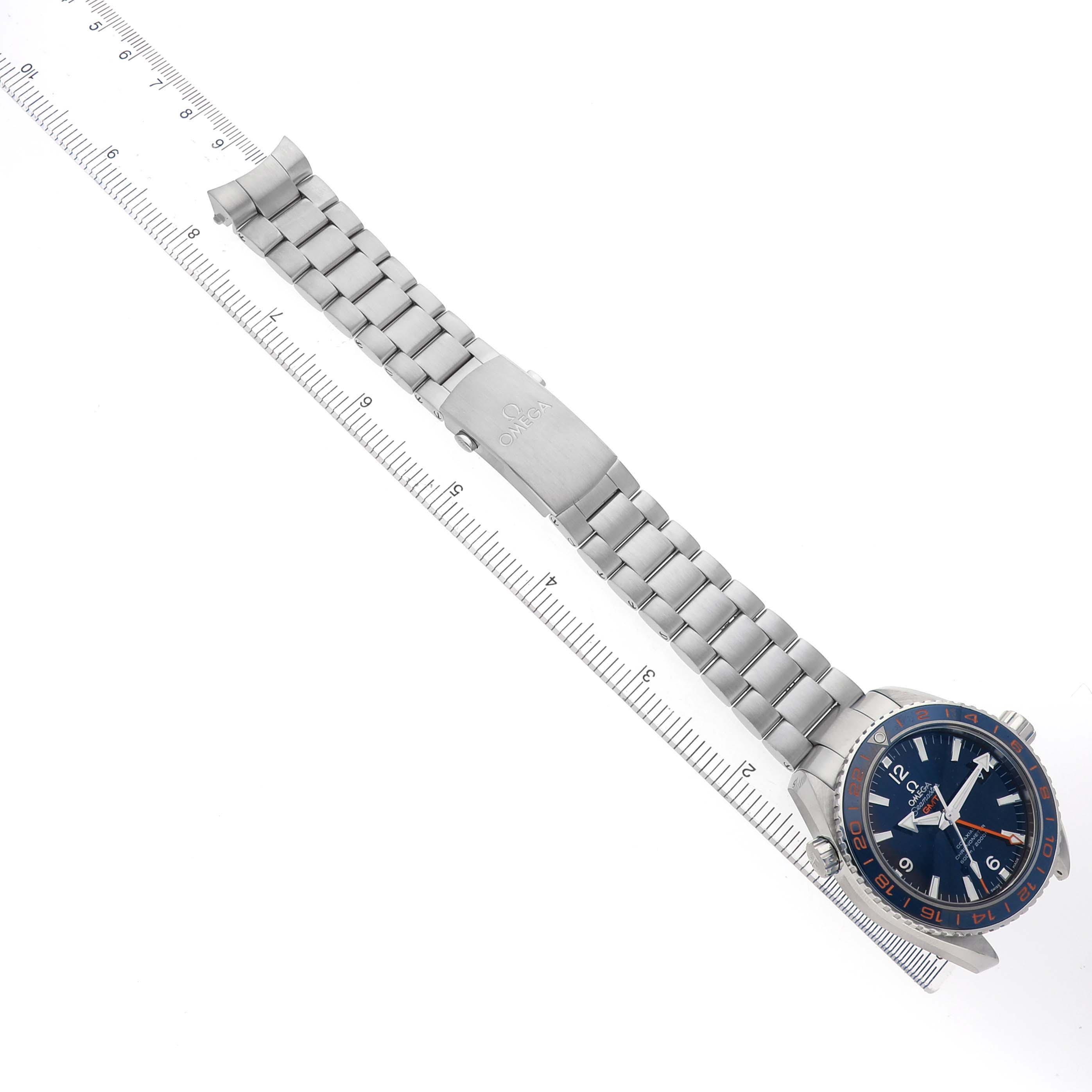 The Omega Planet Ocean 232.30.44.22.03.001 Men's Stainless Steel Blue Dial watch is shown flat, highlighting the steel bracelet and face beside a measuring ruler.