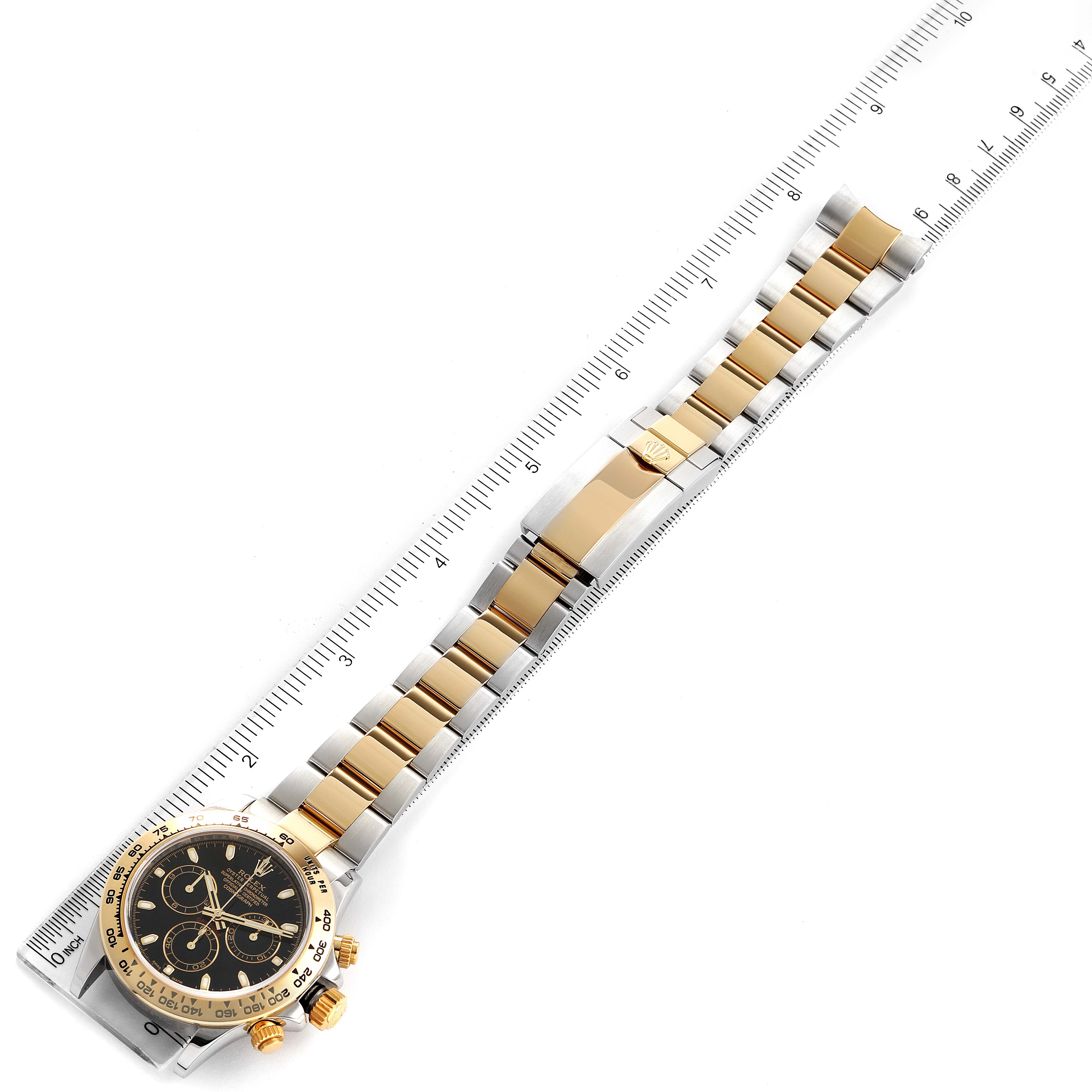 The image shows a top-down view of a Rolex Daytona 116503 Men's Steel and Gold (two tone) Black Dial 116503 Men's Steel and Gold (two tone) Black Dial watch, focusing on the face, bezel, and bracelet positioned along a ruler.