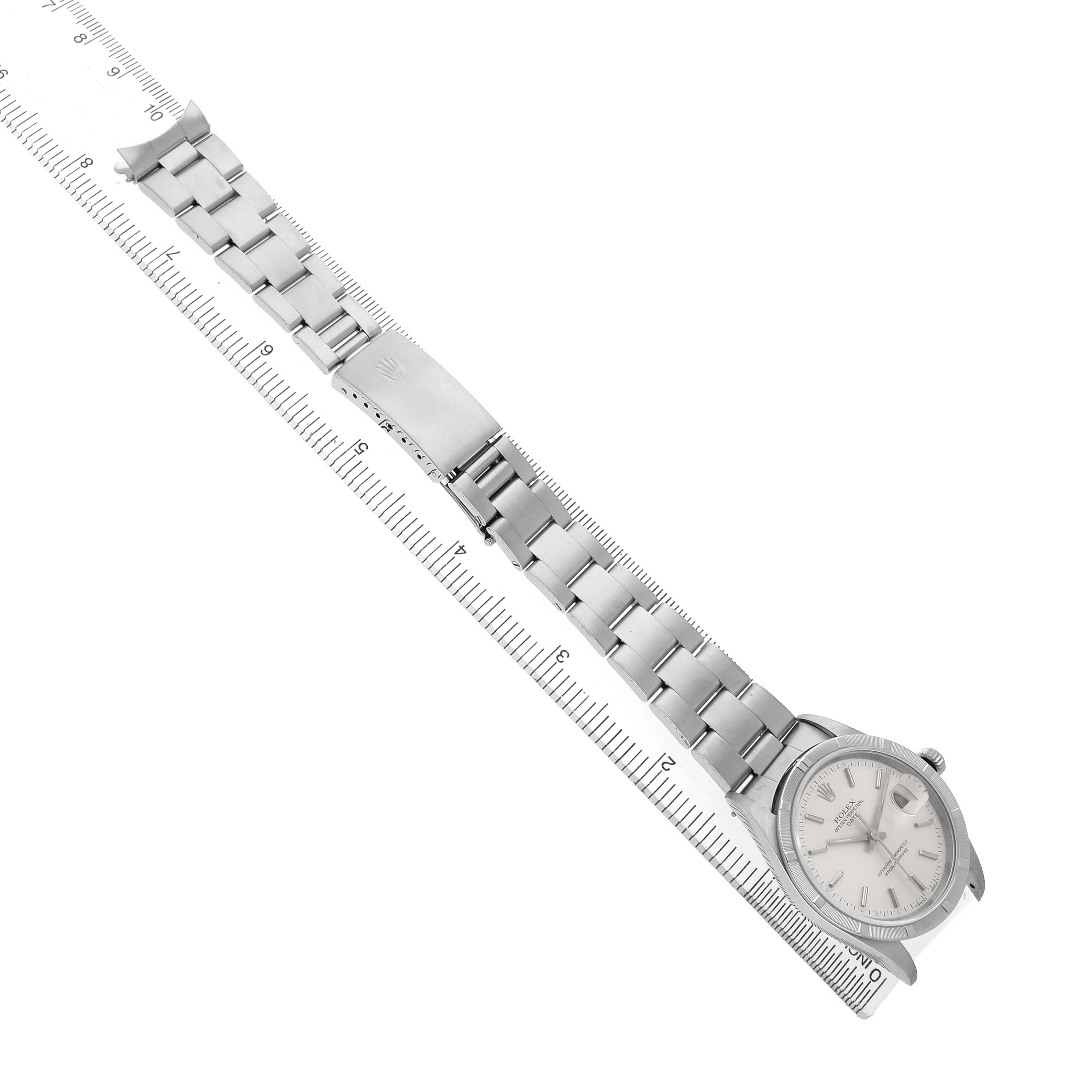 The Rolex Date 15210 Men's Stainless Steel Silver Dial watch is displayed flat, with its face, bracelet, and clasp visible, aligned alongside a ruler.