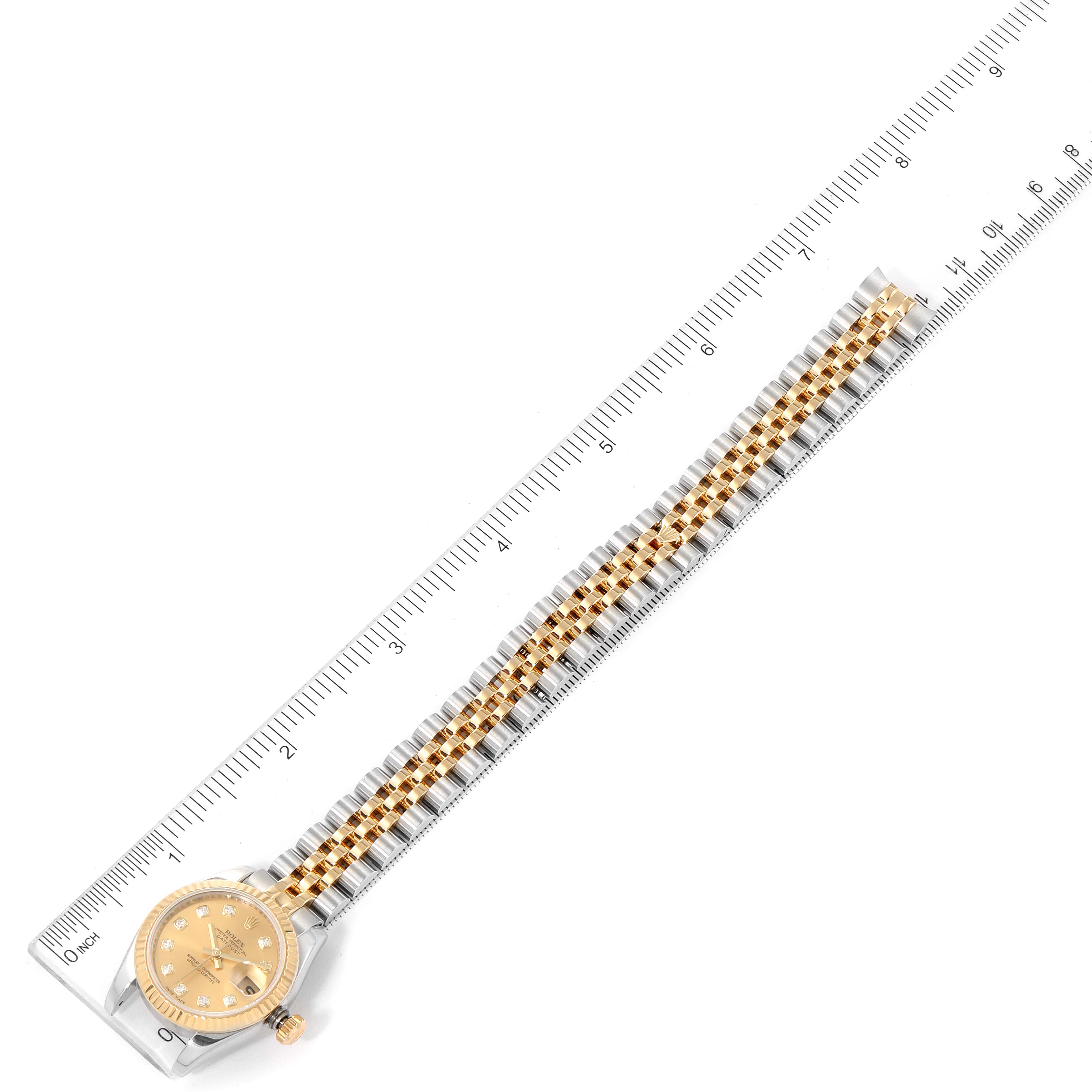 The Rolex Datejust 179173 Women's Steel and Gold (two tone) Champagne Dial 179173 Women's Steel and Gold (two tone) Champagne Dial watch is shown from a top-down angle, featuring its dial, case, and full bracelet against a ruler.