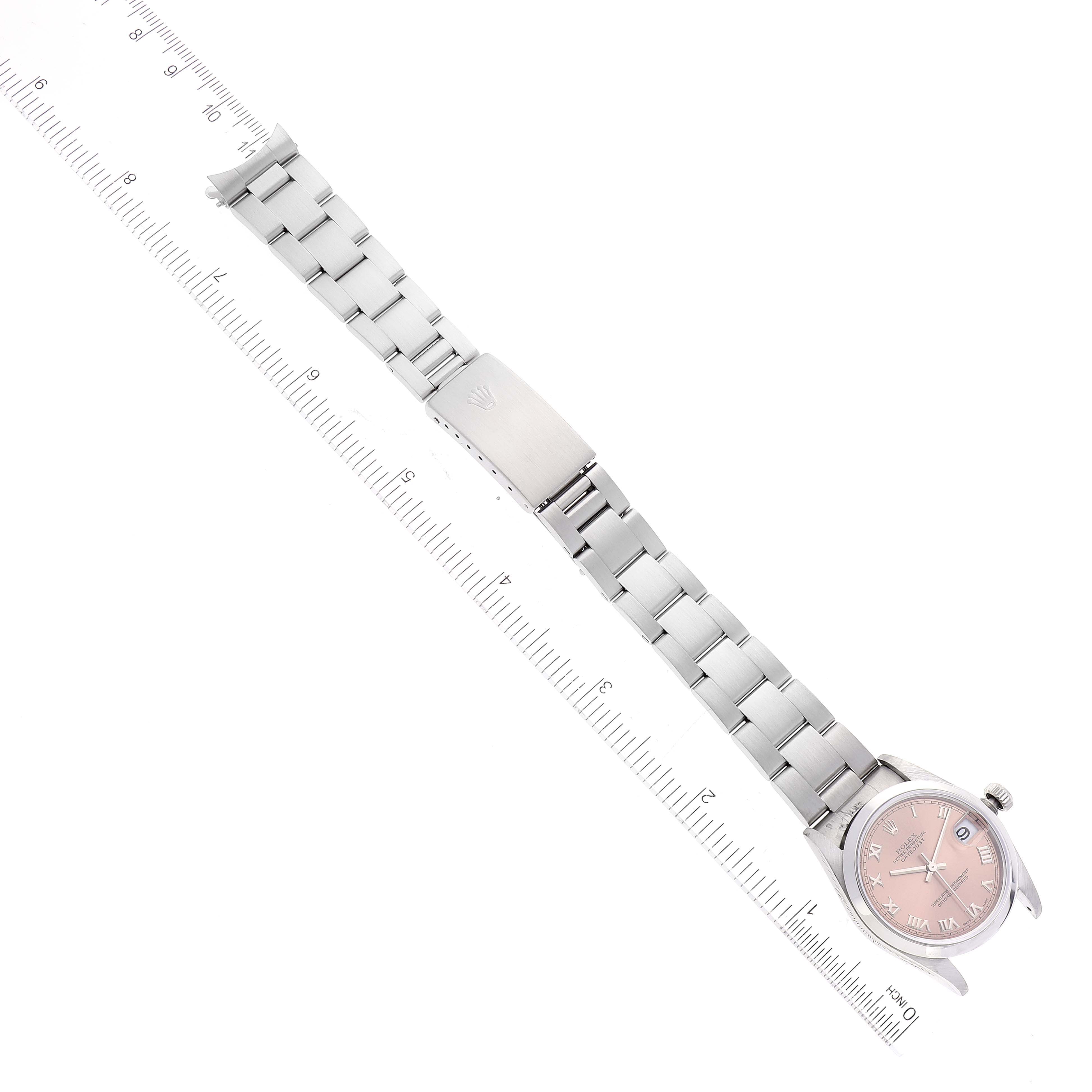 The image shows a full view of a Rolex Mid-Size 78240 Women
s Stainless Steel Pink Dial 78240 Women
s Stainless Steel Pink Dial model watch with a pink dial and a metal bracelet, next to a measuring ruler.