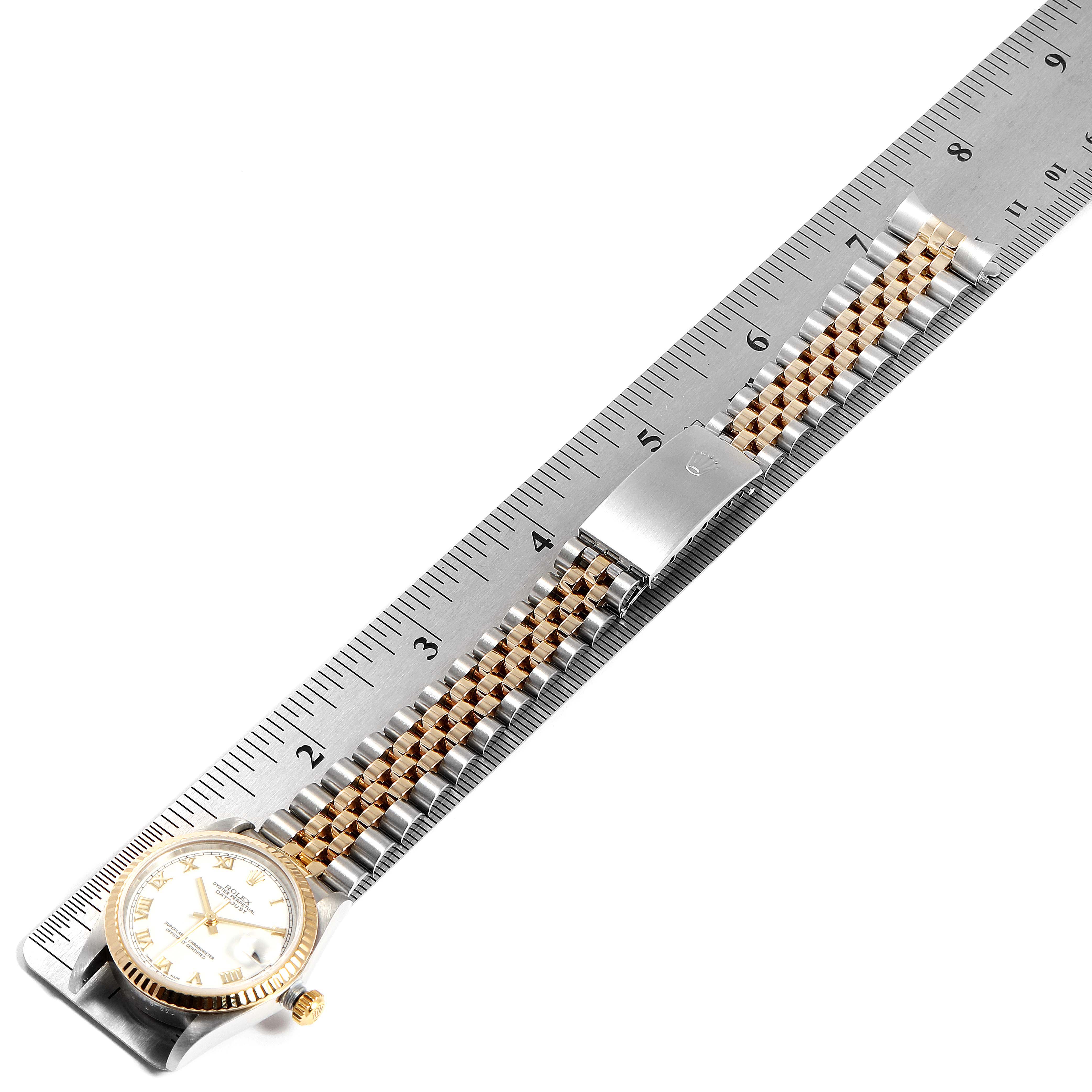 The image shows a side angle of a Rolex Mid-Size 78273 Women
s Steel and Gold (two tone) White Dial 78273 Women
s Steel and Gold (two tone) White Dial watch, highlighting its dial, bezel, crown, and two-tone bracelet with a clasp, placed next to a ruler.