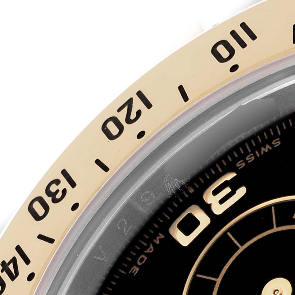 The image shows a close-up of the bezel and part of the dial of a Rolex Daytona 116523 Men
s Steel and Gold (two tone) Black Dial 116523 Men
s Steel and Gold (two tone) Black Dial watch.