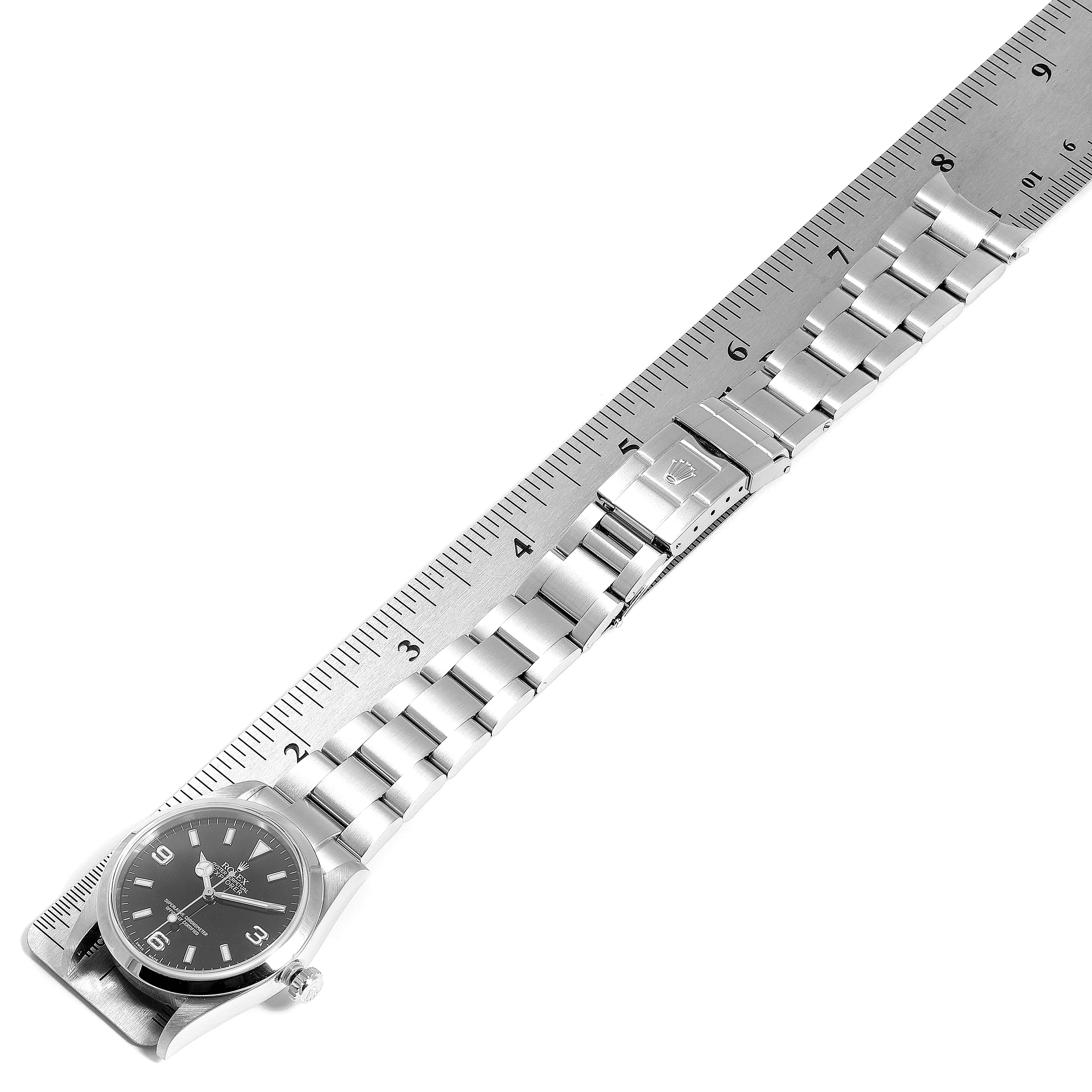 The image shows a top view of a Rolex Explorer 114270 Men
s Stainless Steel Black Dial 114270 Men
s Stainless Steel Black Dial watch with its metal band extended next to a measuring ruler.