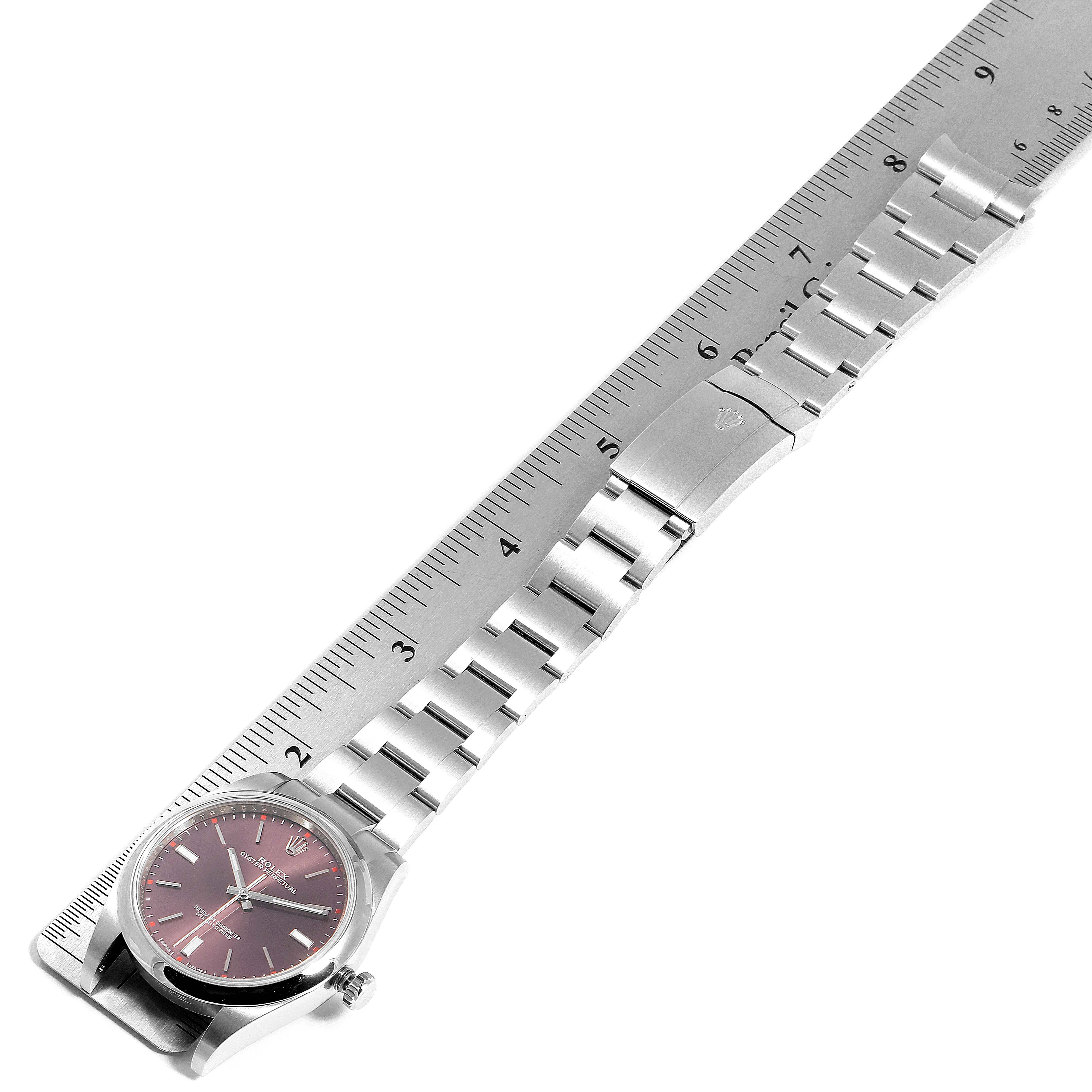 The Rolex Oyster Perpetual 114300 Men's Stainless Steel Burgundy Dial 114300 Men's Stainless Steel Burgundy Dial watch is shown from a top view, displaying the face, bracelet, and clasp alongside a measuring ruler.