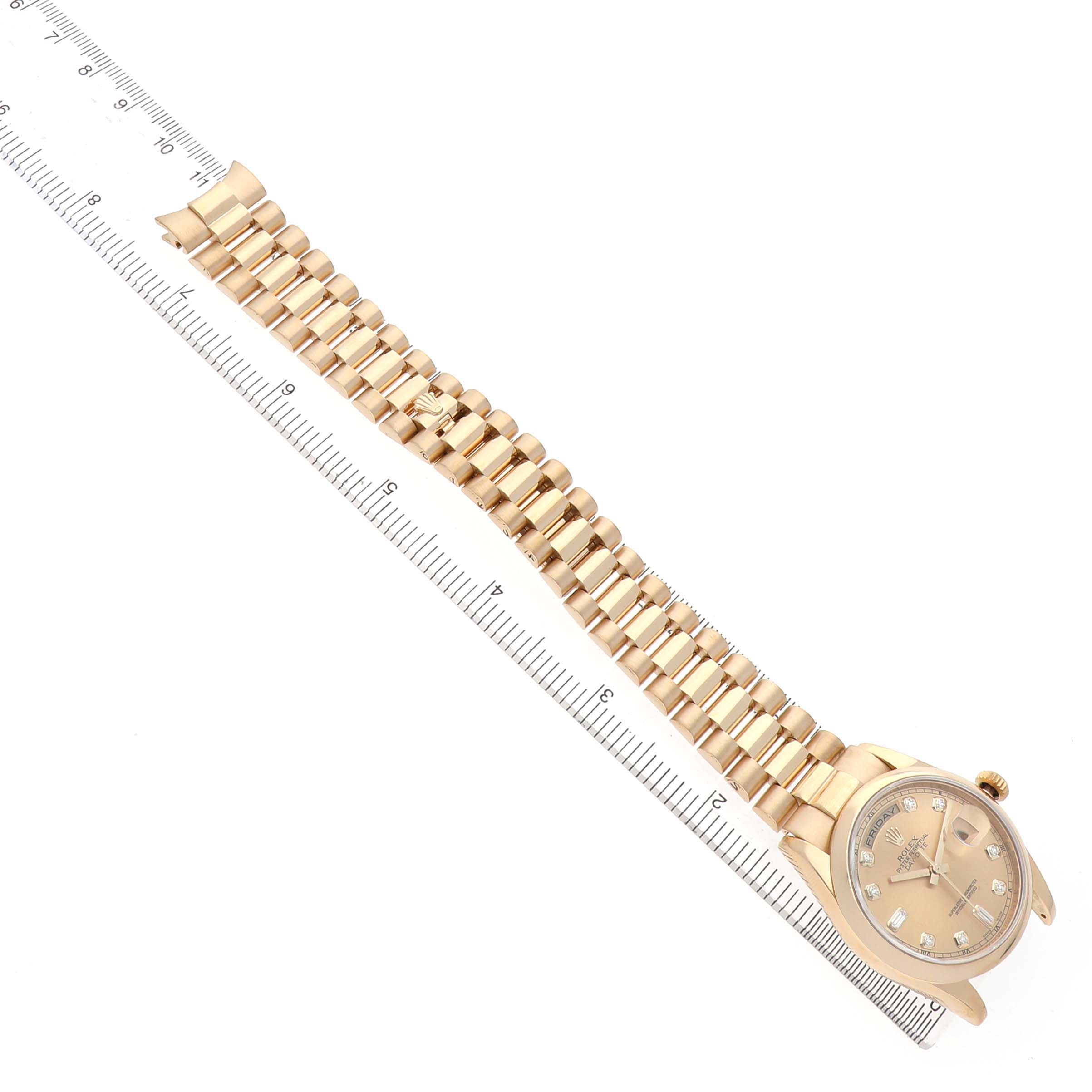 The Rolex President 118208 Men's Yellow Gold Champagne Dial model watch is shown from a top view, displaying its dial, bezel, and full bracelet alongside a ruler for scale.