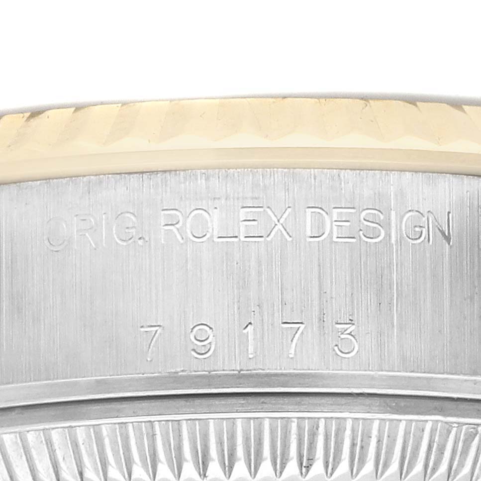 The image shows a partial view of the case side of a Rolex Datejust 79173 Women's Steel and Gold (two tone) Champagne Dial watch, featuring engraved text and part of the fluted bezel.