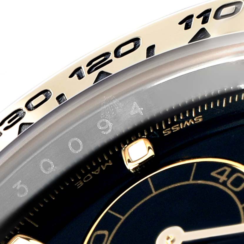 The image shows a close-up of the bezel and part of the dial on a Rolex Daytona 116503 Men
s Steel and Gold (two tone) Black Dial, highlighting the tachymetric scale and hour markers.