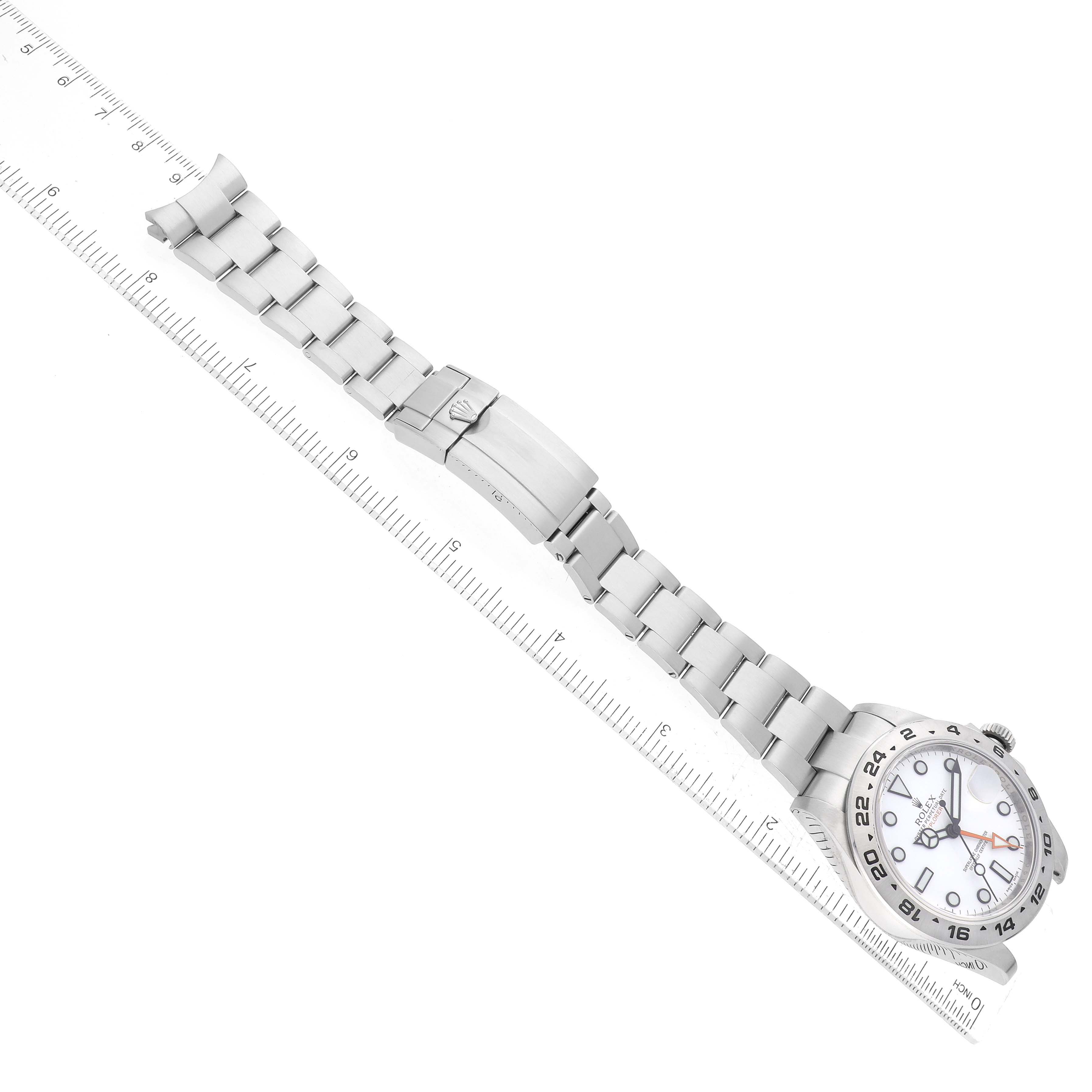 The image shows a Rolex Explorer 216570 Men's Stainless Steel White Dial 216570 Men's Stainless Steel White Dial watch laid flat at a diagonal angle with its full bracelet and clasp visible next to a ruler.