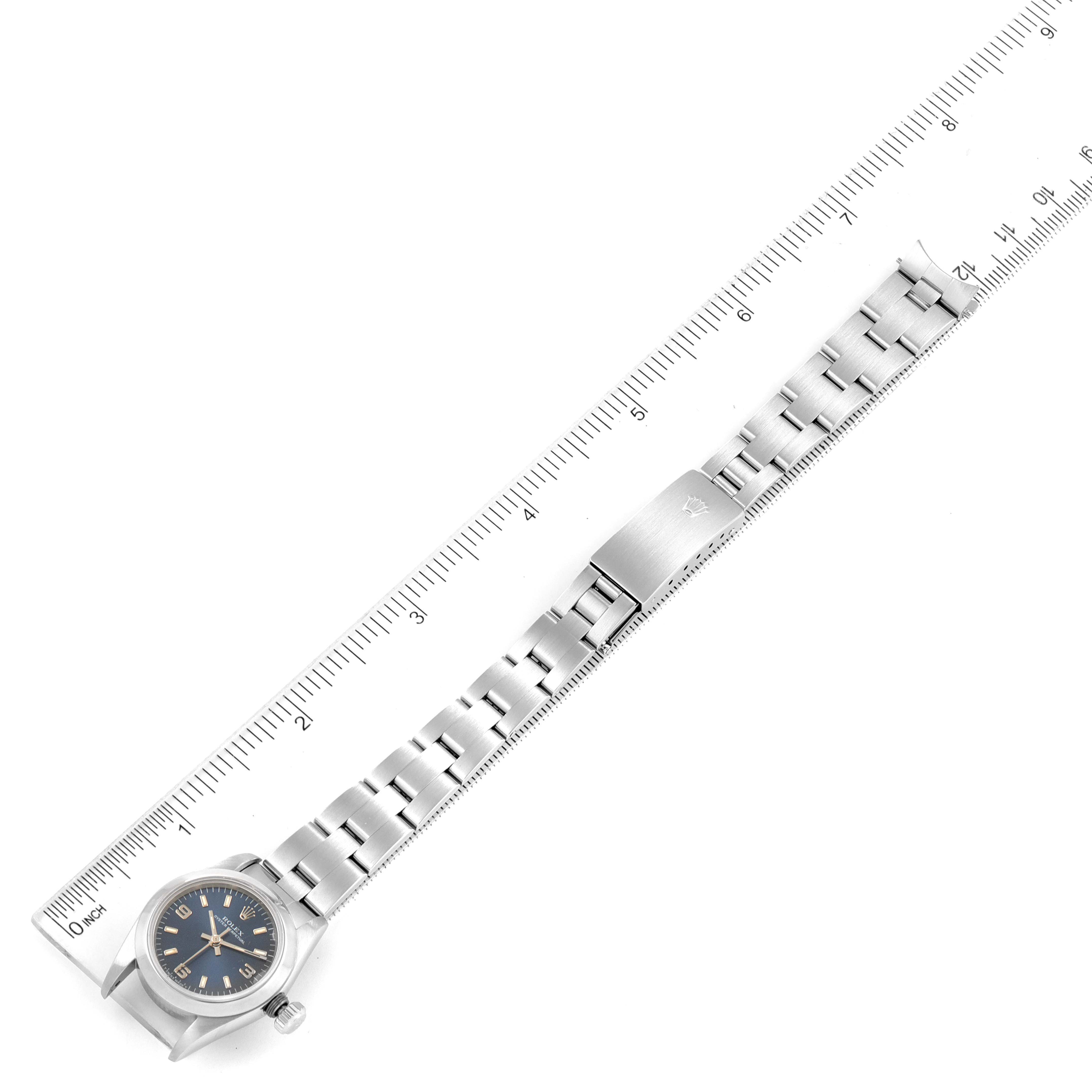 This image shows the Rolex Oyster Perpetual 67180 Women's Stainless Steel Blue Dial 67180 Women's Stainless Steel Blue Dial watch laid flat next to a ruler, displaying the full length of the bracelet and clasp.