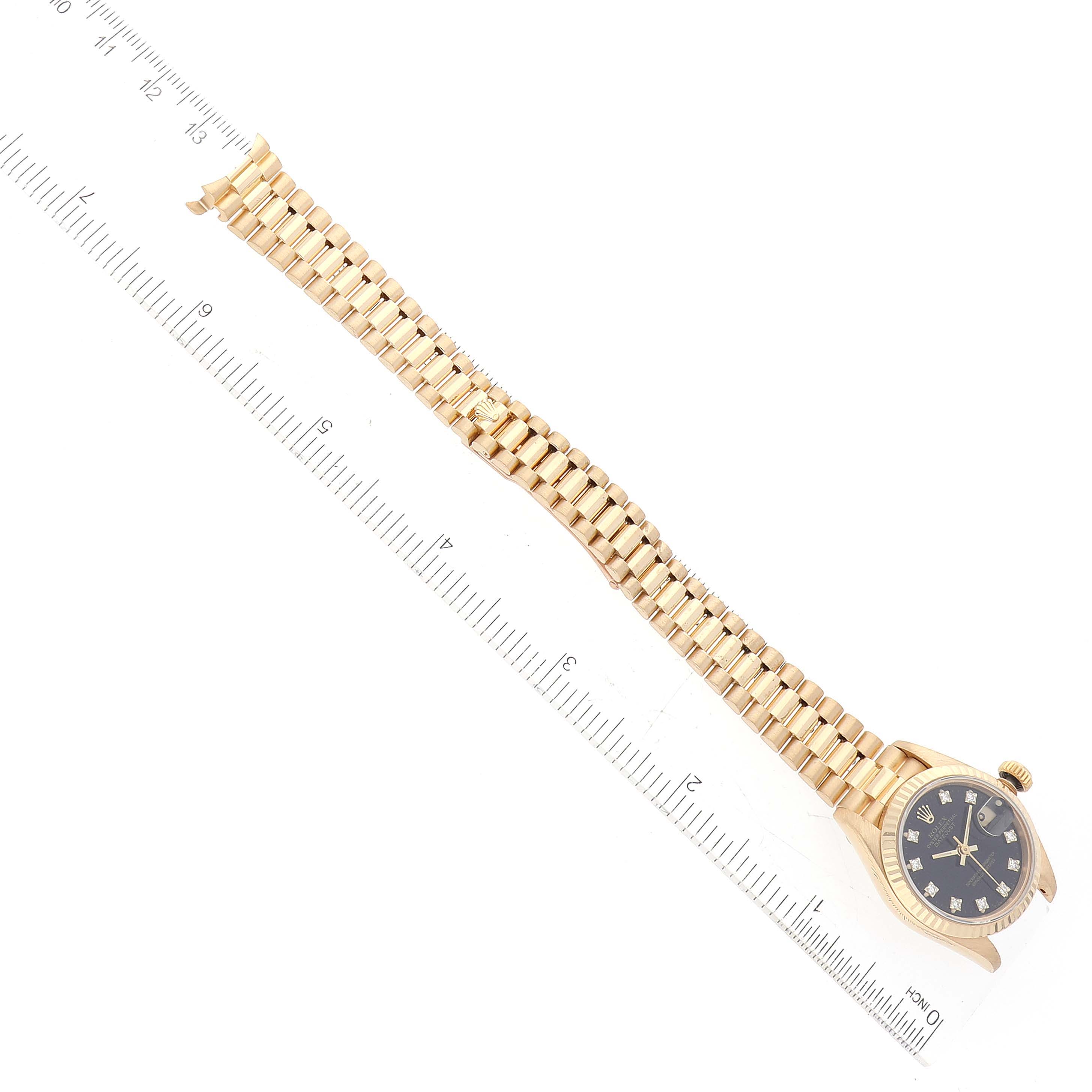 This image shows a Rolex President 69178 Women's Yellow Gold Black Dial 69178 Women's Yellow Gold Black Dial model watch from an overhead angle with the ruler displaying its length.