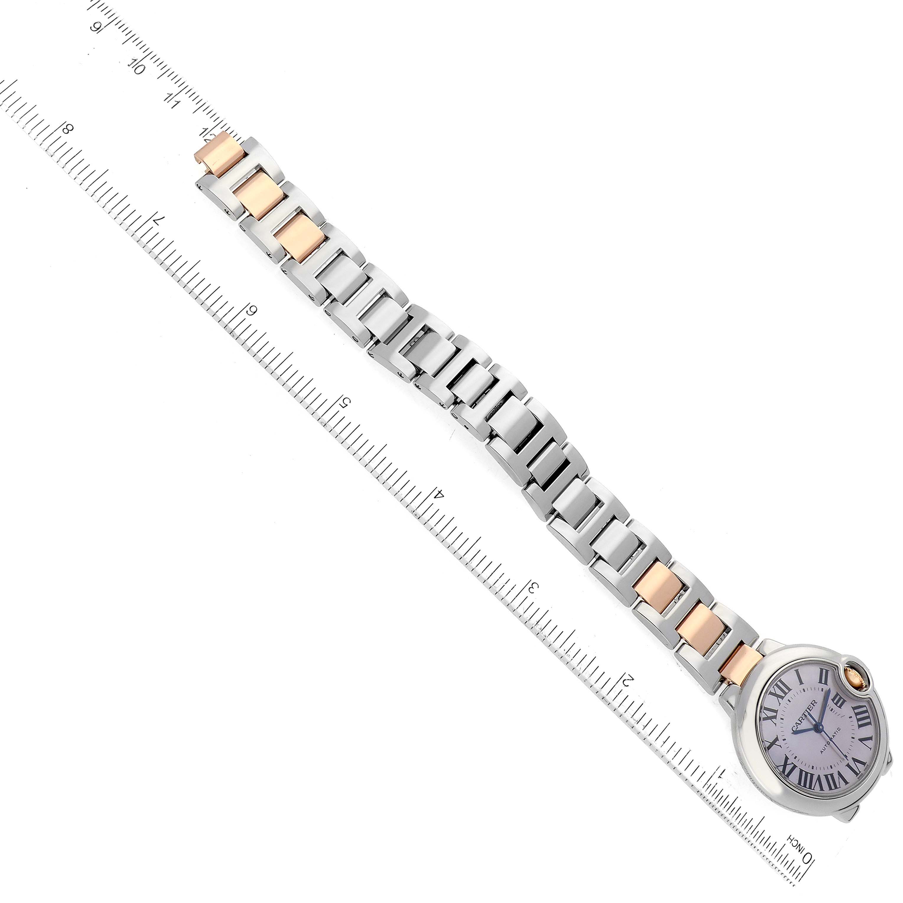 This image shows a side view of a Cartier Ballon Bleu W6920098 Women's Steel and Gold (two tone) Mother of Pearl Dial W6920098 Women's Steel and Gold (two tone) Mother of Pearl Dial watch, displaying its face, two-tone bracelet, and a measuring ruler alongside.