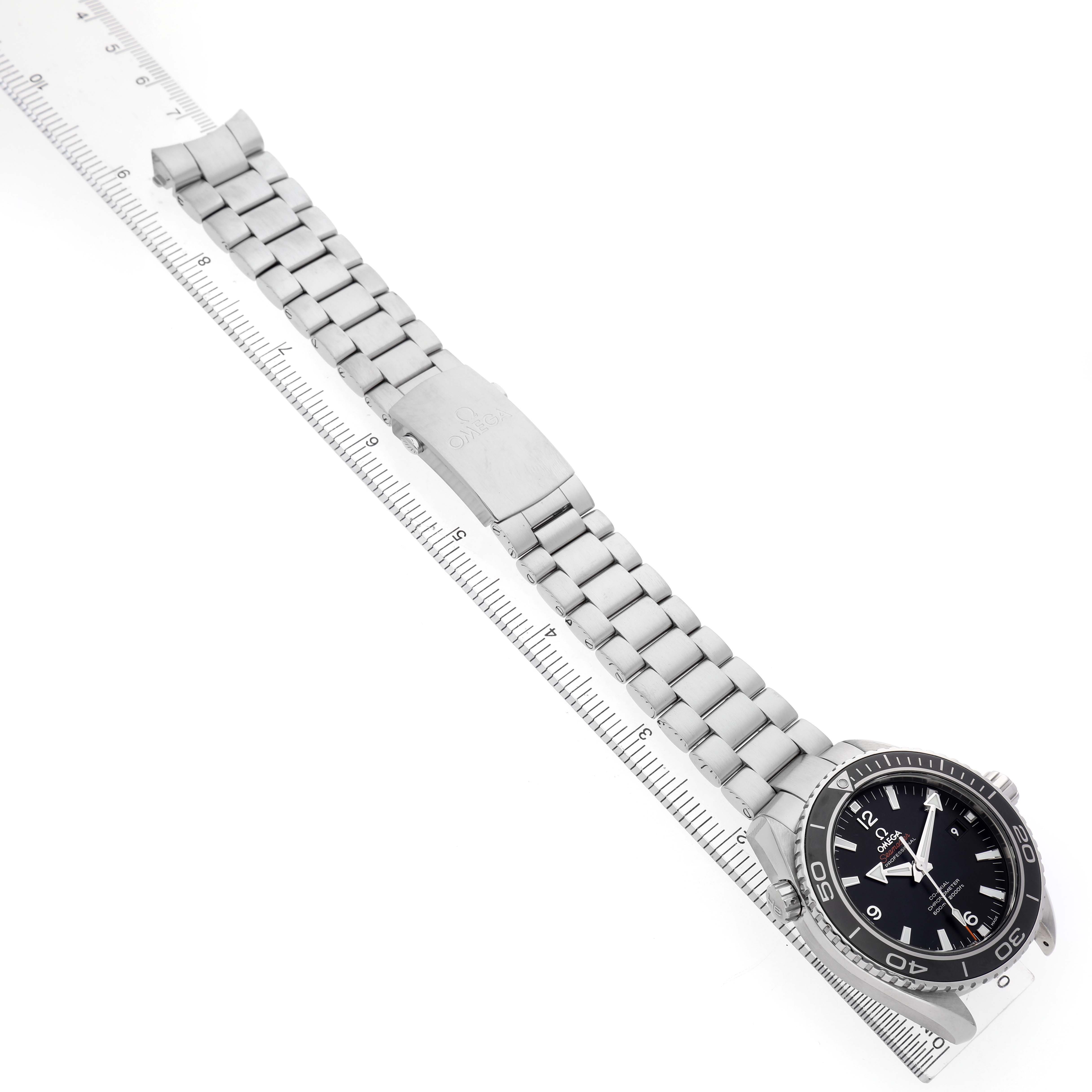 The Omega Planet Ocean 232.30.46.21.01.001 Men's Stainless Steel Black Dial watch is shown from a top-down angle, displaying the dial, bezel, and metal bracelet along with a ruler.