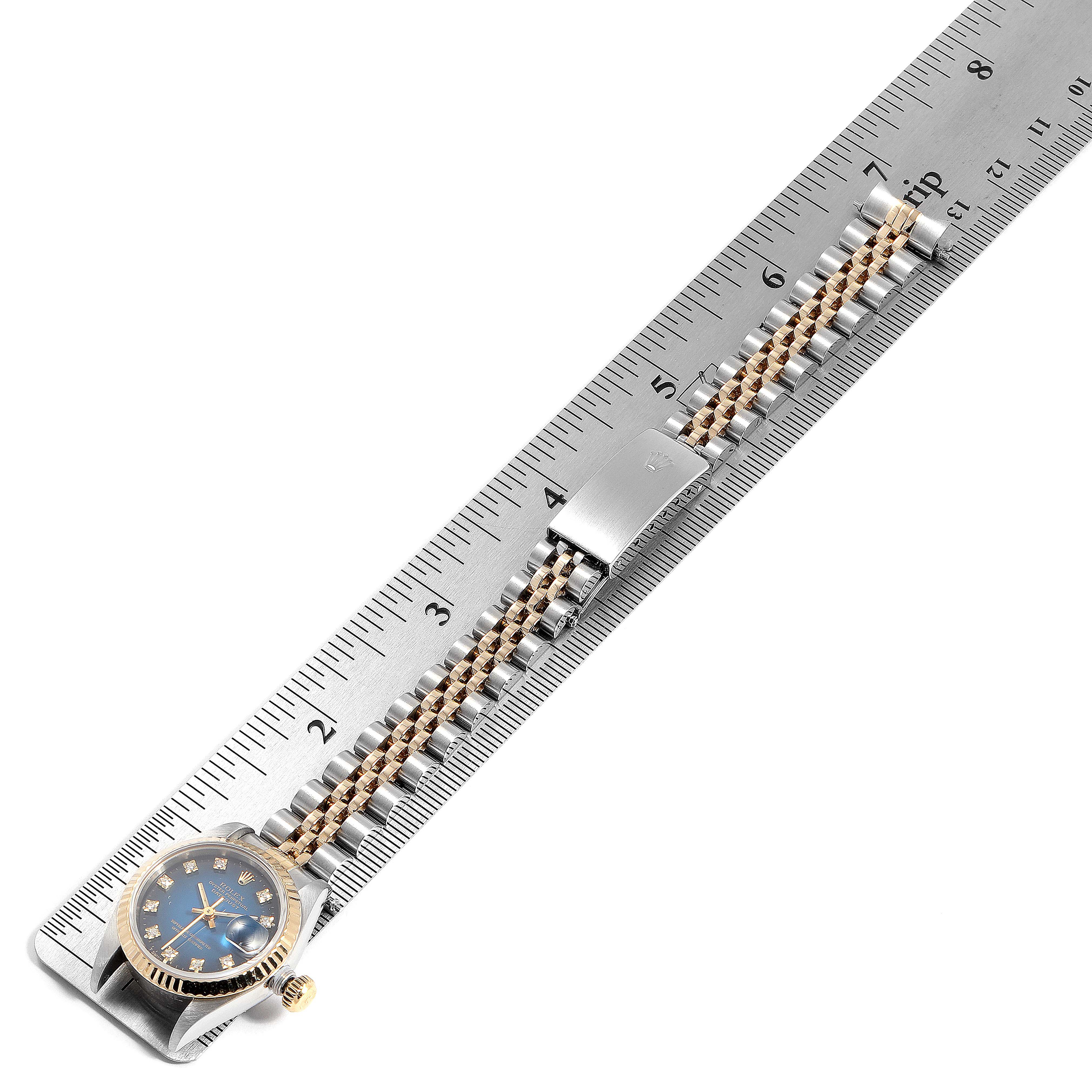 The Rolex Datejust 69173 Women's Steel and Gold (two tone) Blue Dial 69173 Women's Steel and Gold (two tone) Blue Dial watch is shown laid flat next to a ruler, displaying its face, bezel, and bracelet with a clasp.