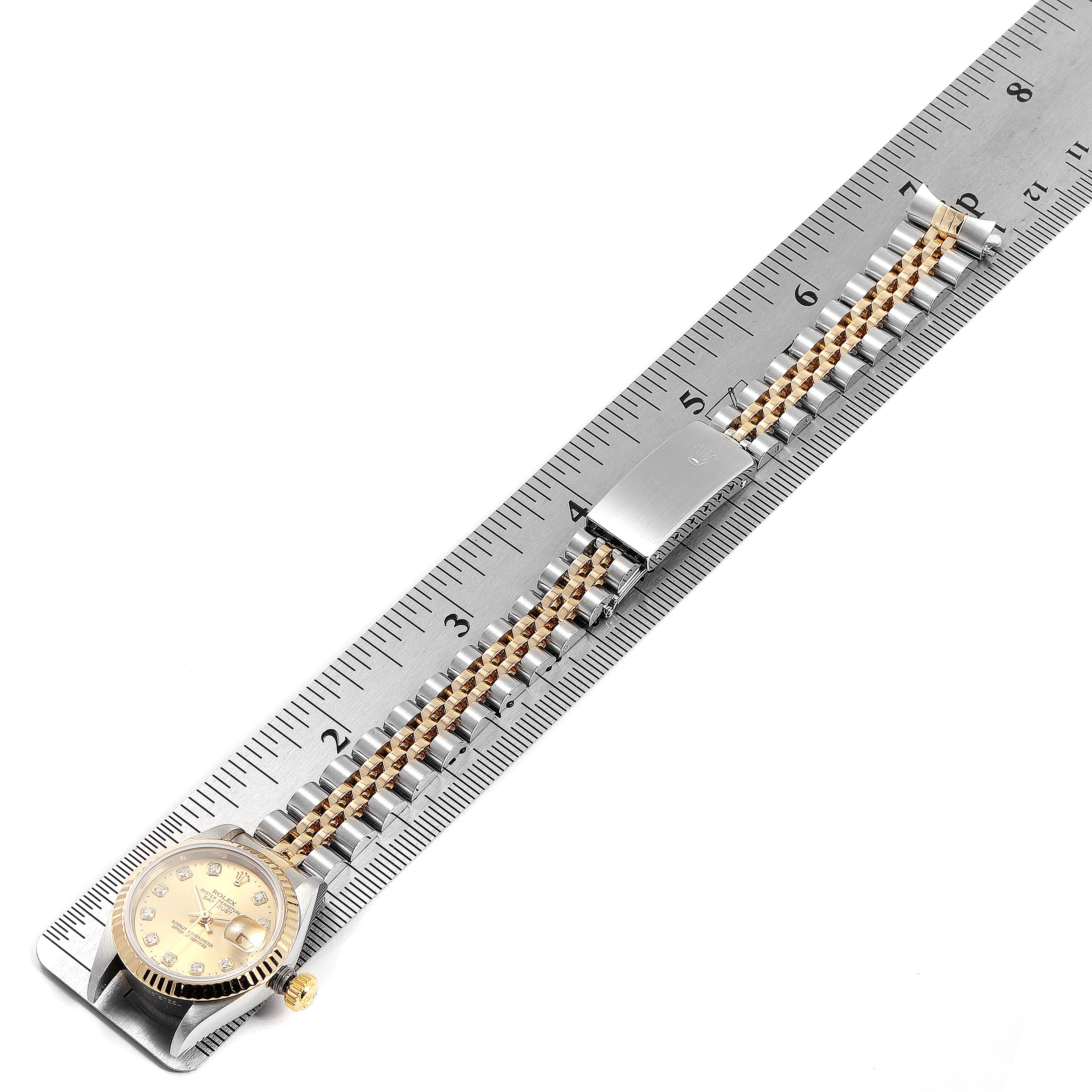 The Rolex Datejust 69173 Women
s Steel and Gold (two tone) Champagne Dial 69173 Women
s Steel and Gold (two tone) Champagne Dial watch is shown from a top-down angle, displaying the face, bracelet, and clasp next to a ruler.