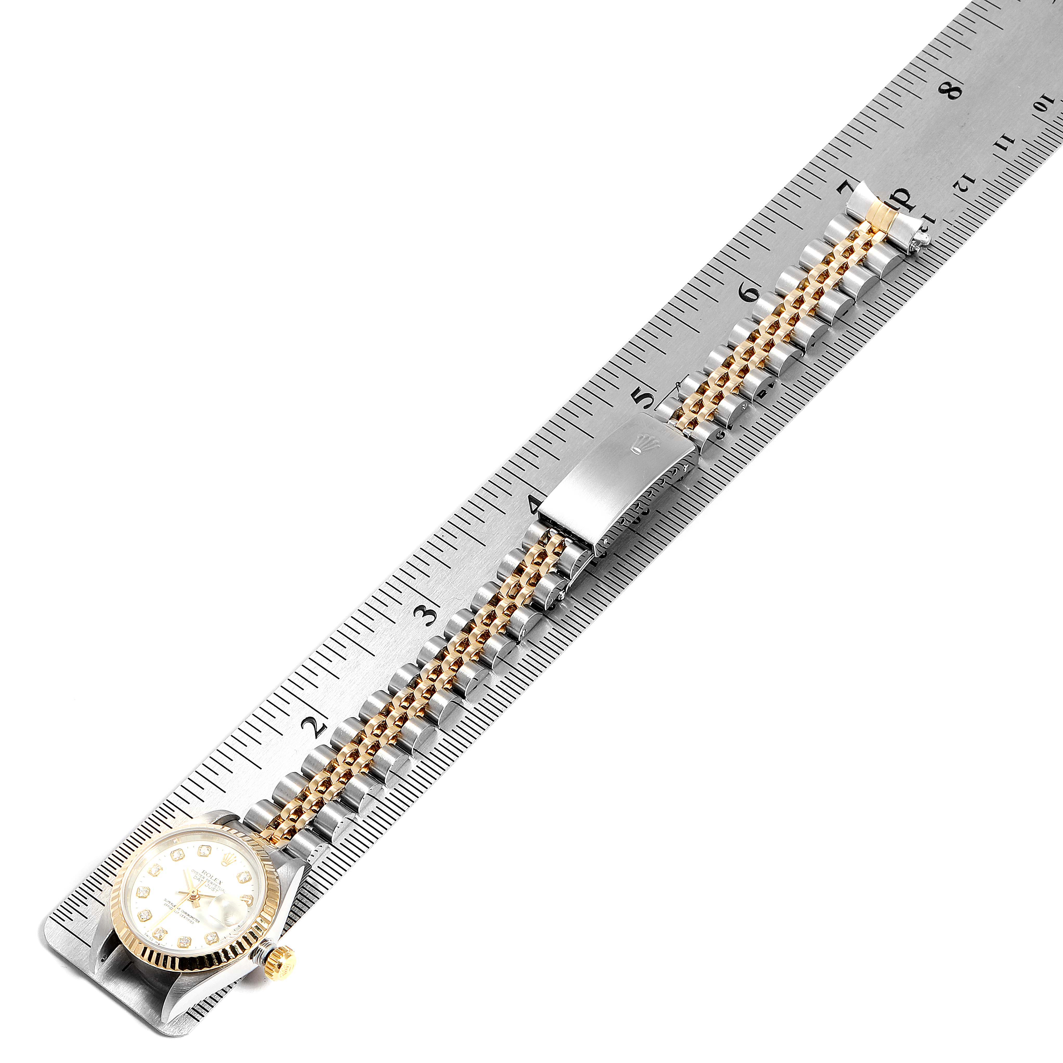 The image shows a Rolex Datejust 69173 Women
s Steel and Gold (two tone) White Dial 69173 Women
s Steel and Gold (two tone) White Dial watch laid flat against a ruler, displaying its face, bracelet, and clasp from a top-down angle.