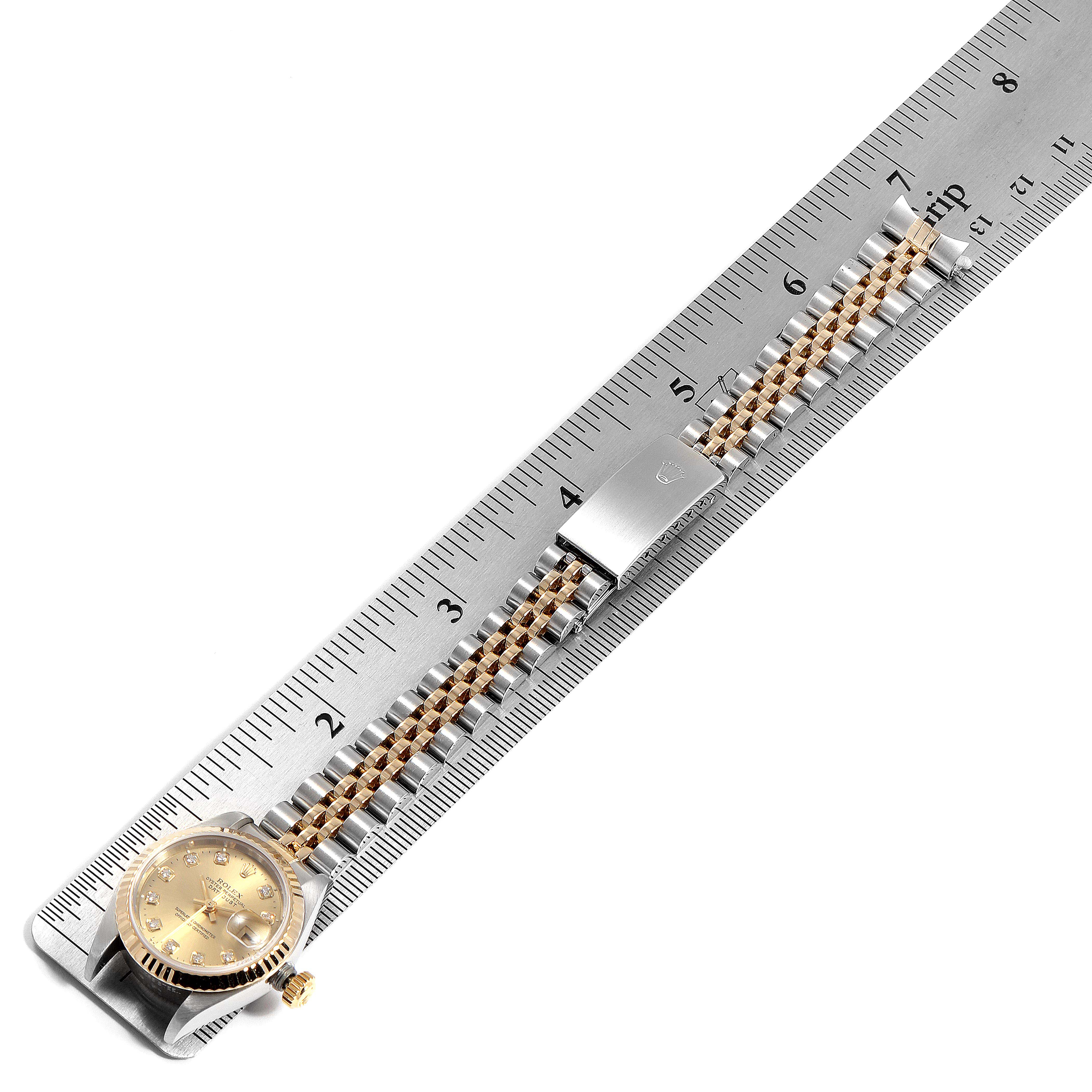 The Rolex Datejust 79173 Women's Steel and Gold (two tone) Champagne Dial 79173 Women's Steel and Gold (two tone) Champagne Dial watch is shown flat with its gold and silver chain bracelet aligned with a measuring ruler.