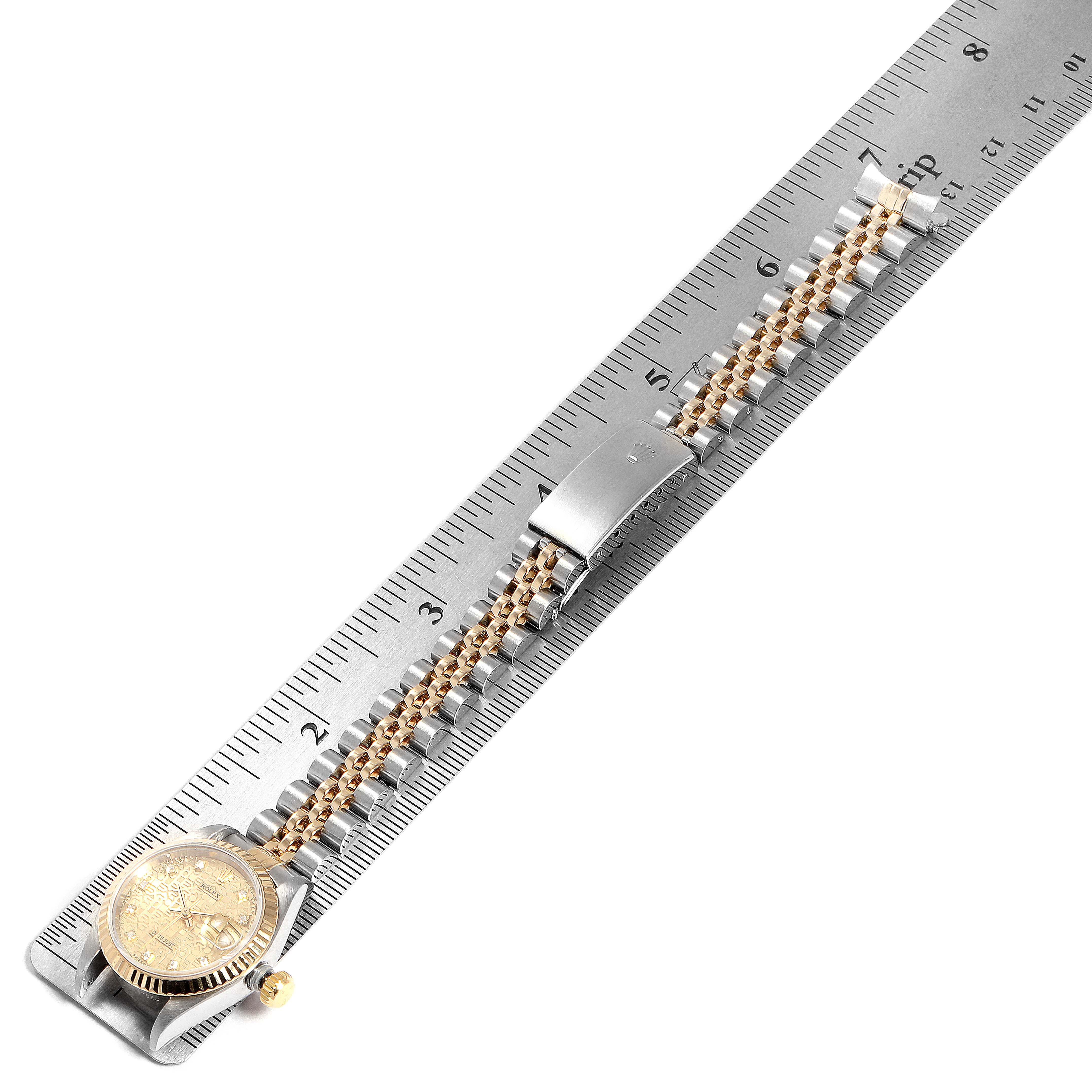 The Rolex Datejust 79173 Women
s Steel and Gold (two tone) Champagne Dial 79173 Women
s Steel and Gold (two tone) Champagne Dial watch is laid flat against a ruler, showing the bracelet, clasp, and partial view of the watch face and crown.