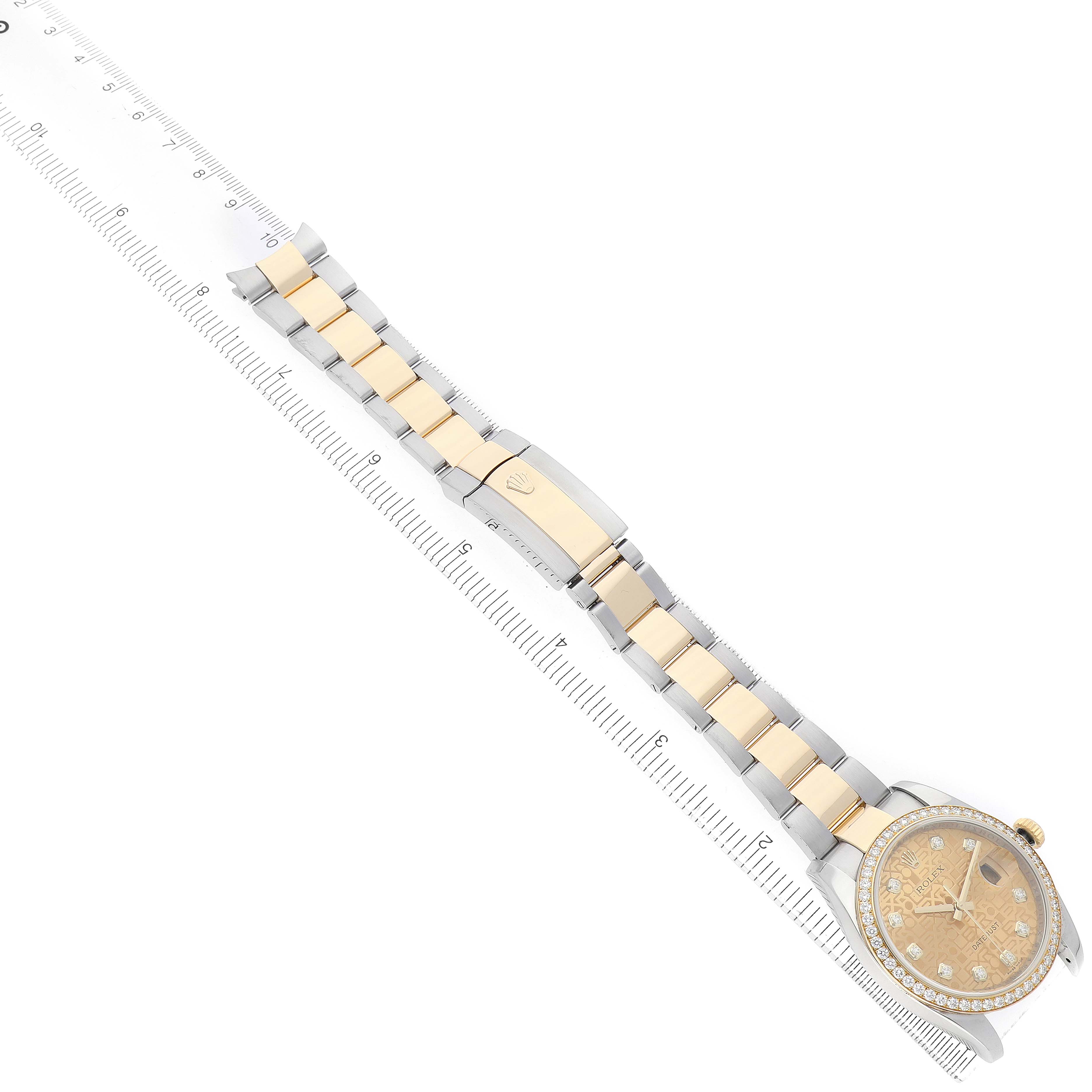 The Rolex Datejust 116243 Men's Steel and Gold (two tone) Champagne Dial is shown from a top-down angle, displaying the dial, bezel, and full bracelet with a folding clasp alongside a ruler.