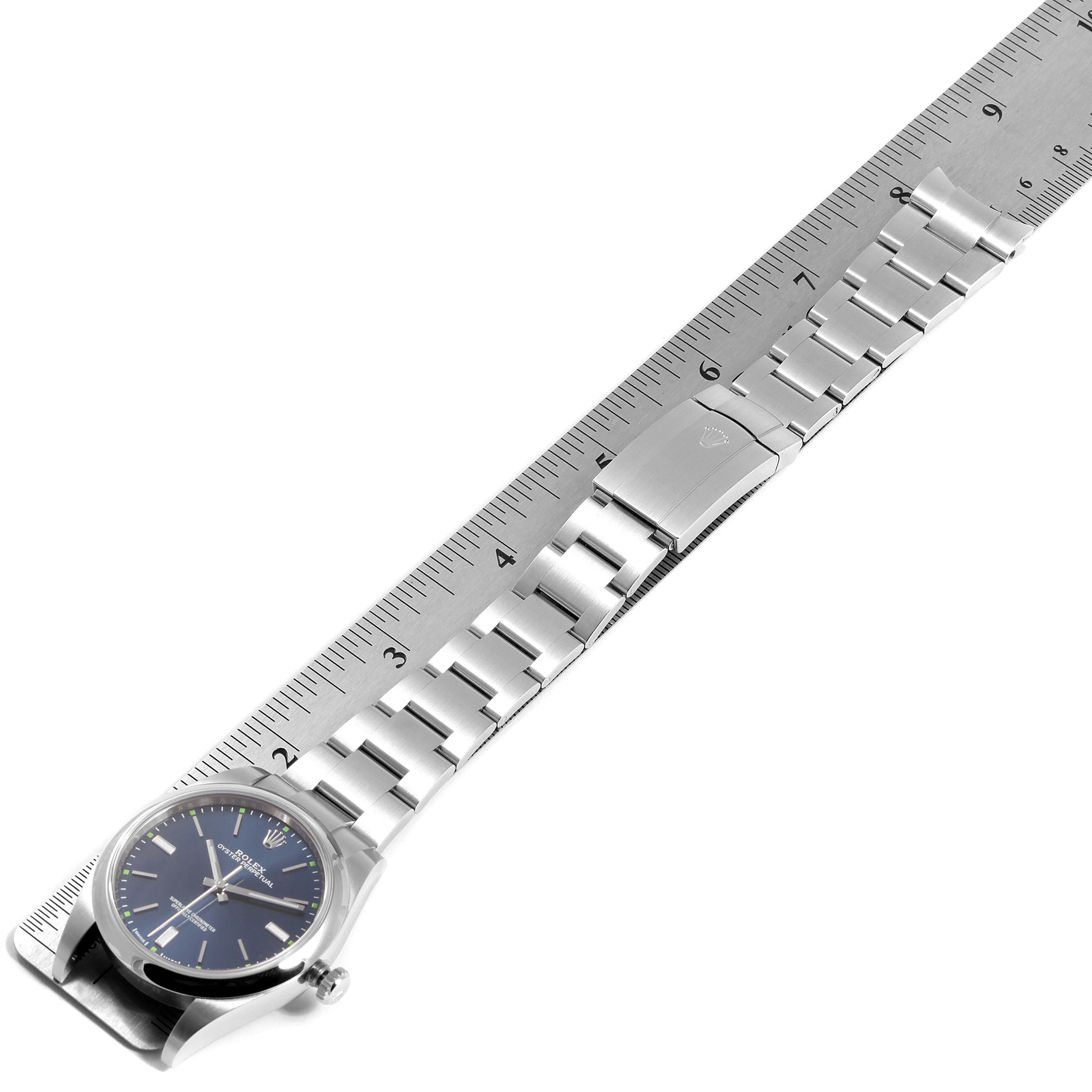 The Rolex Oyster Perpetual 114300 Men's Stainless Steel Blue Dial 114300 Men's Stainless Steel Blue Dial watch is shown from an overhead angle, displayed alongside a ruler for size reference.